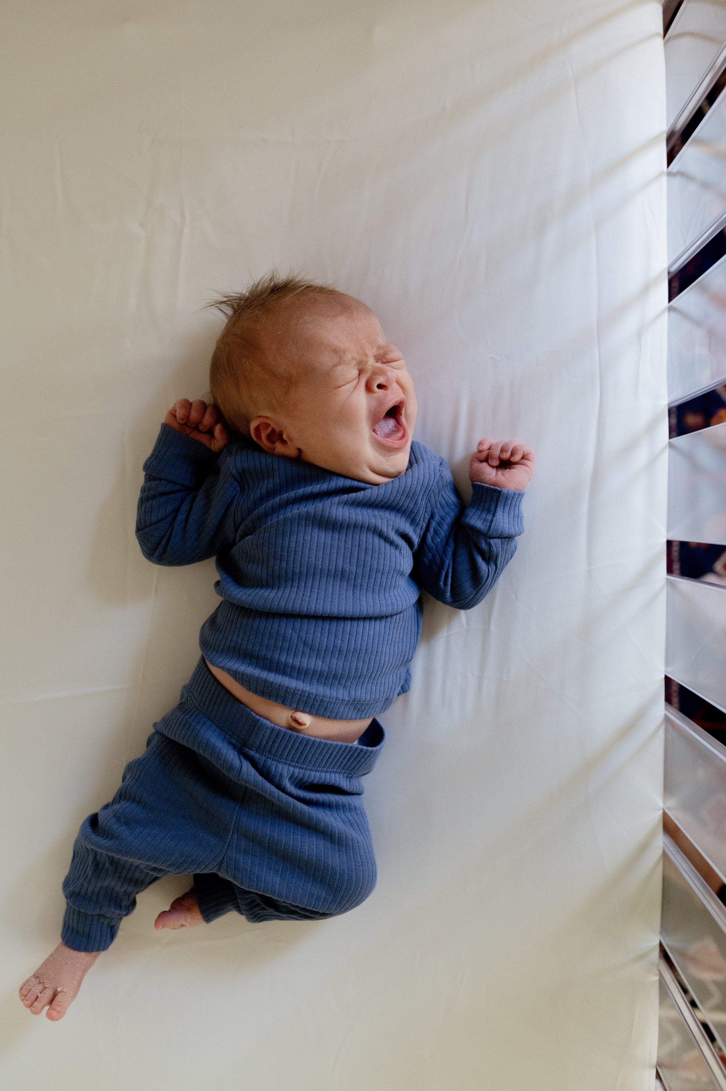 Baby in blue outfit yawns in crib