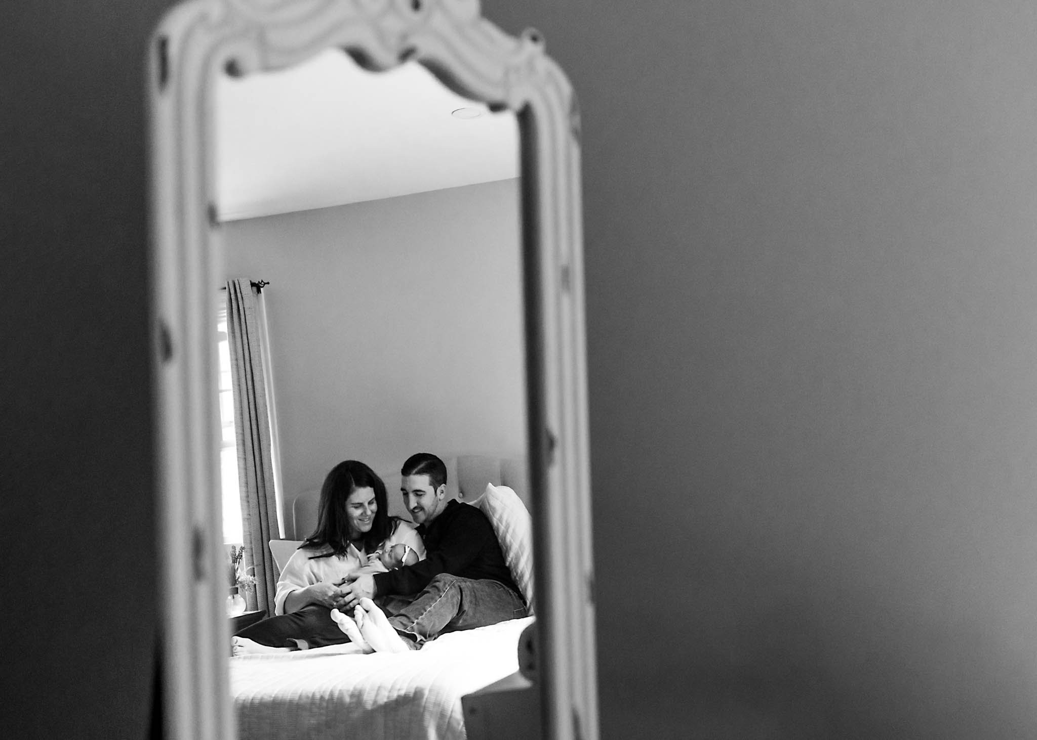 Mirror reflection of parents and baby on bed