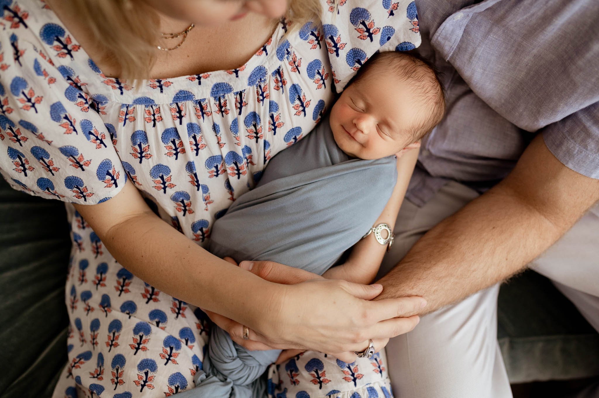 Baby boy in blue wrap snuggles with parents' arms