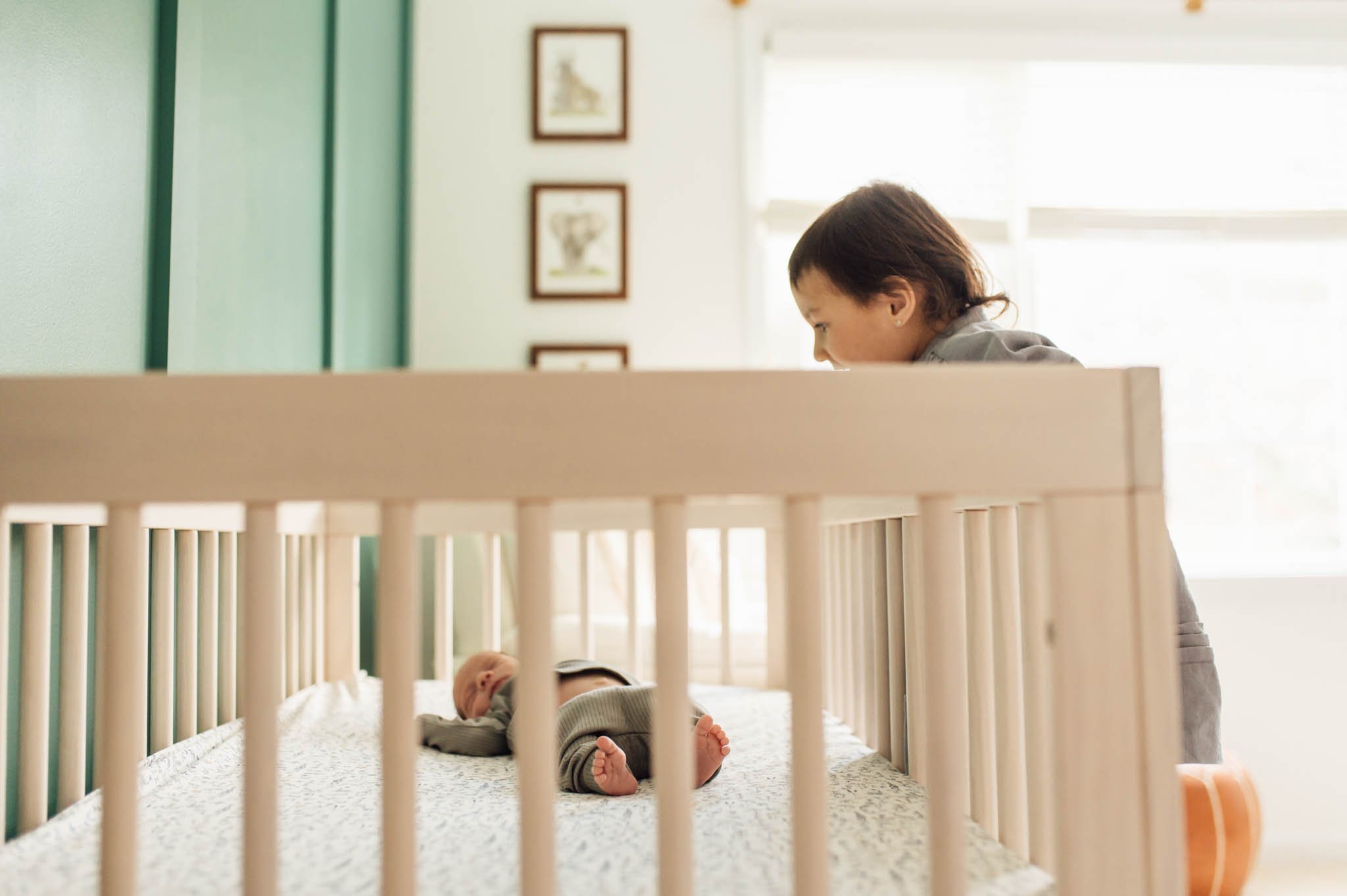 Toddler sister peeks into baby's crib