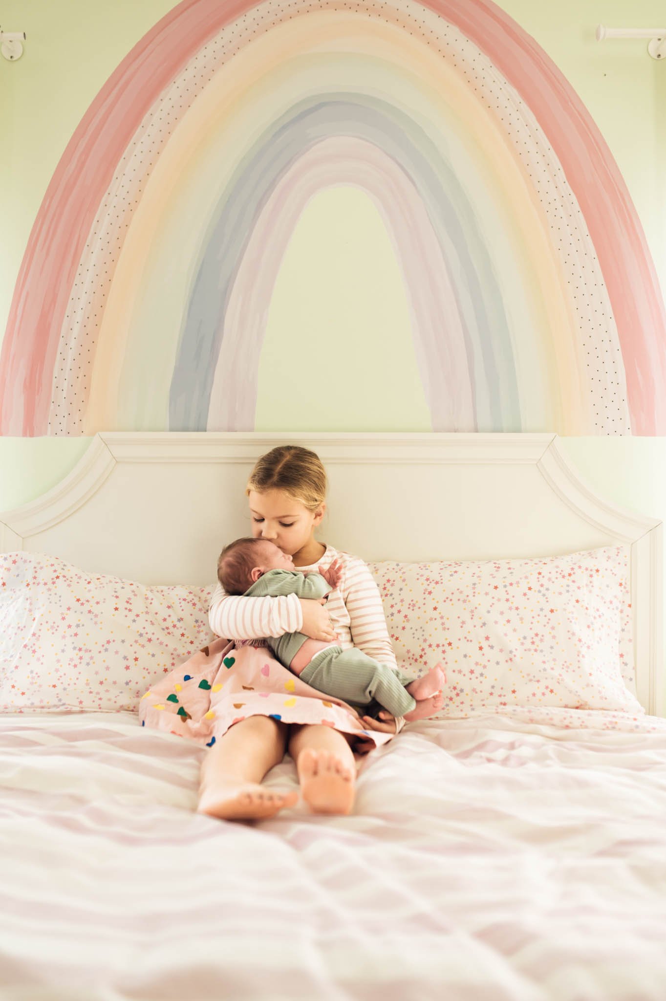 Big sister cuddles baby, rainbow painting