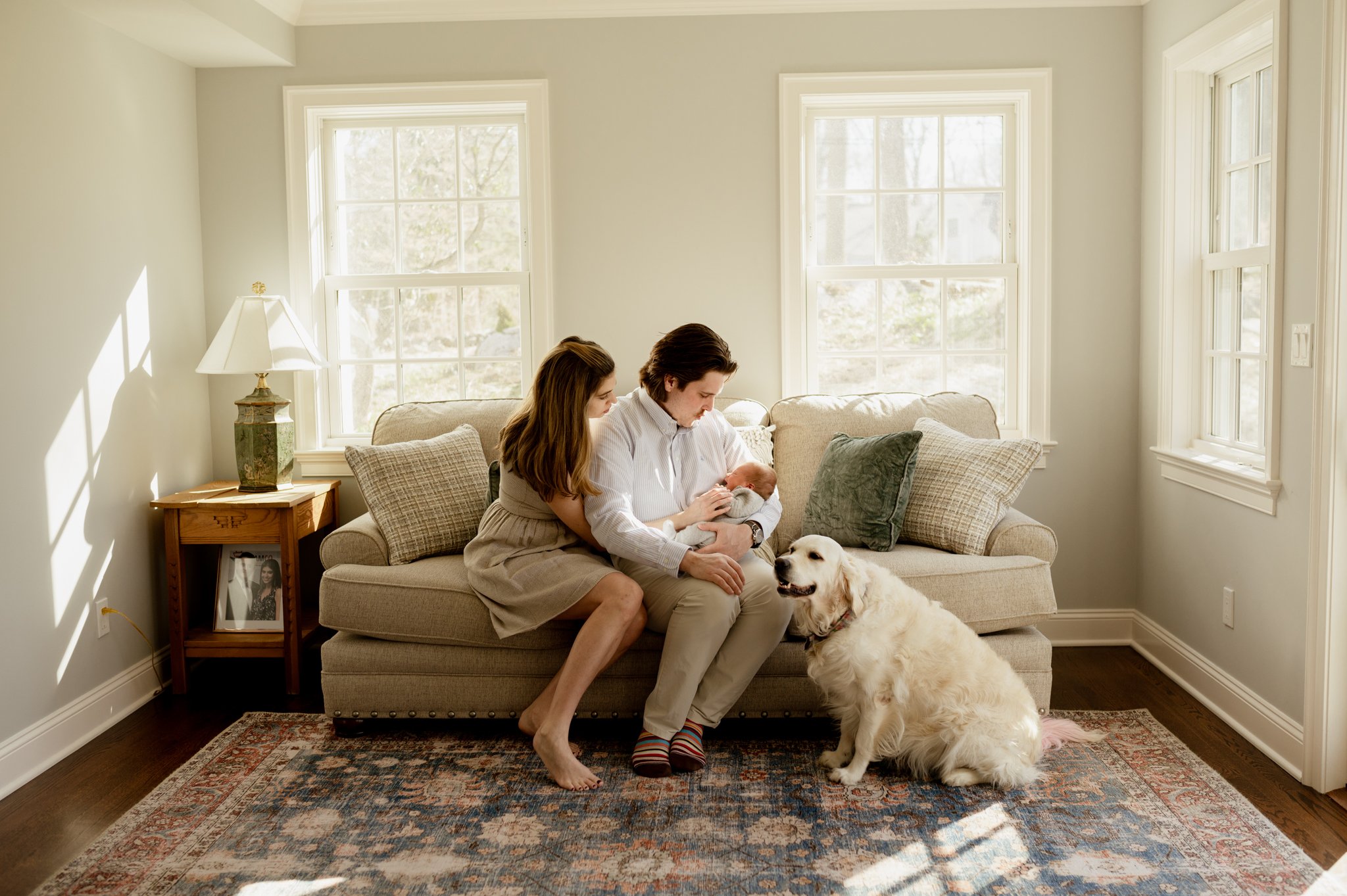 Parents snuggle baby on couch with Labrador