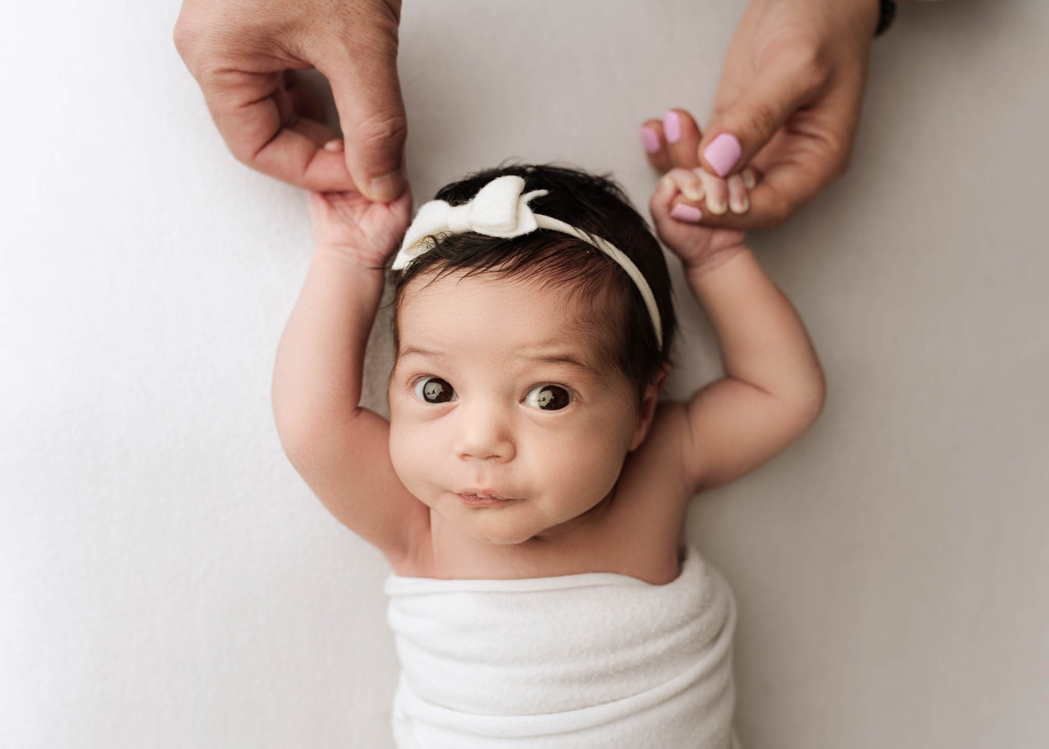 Baby girl in white holding parents' hands