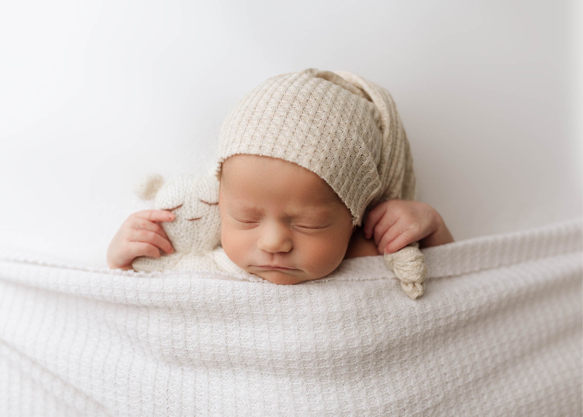 Baby tucked in with hat and teddy, white blanket