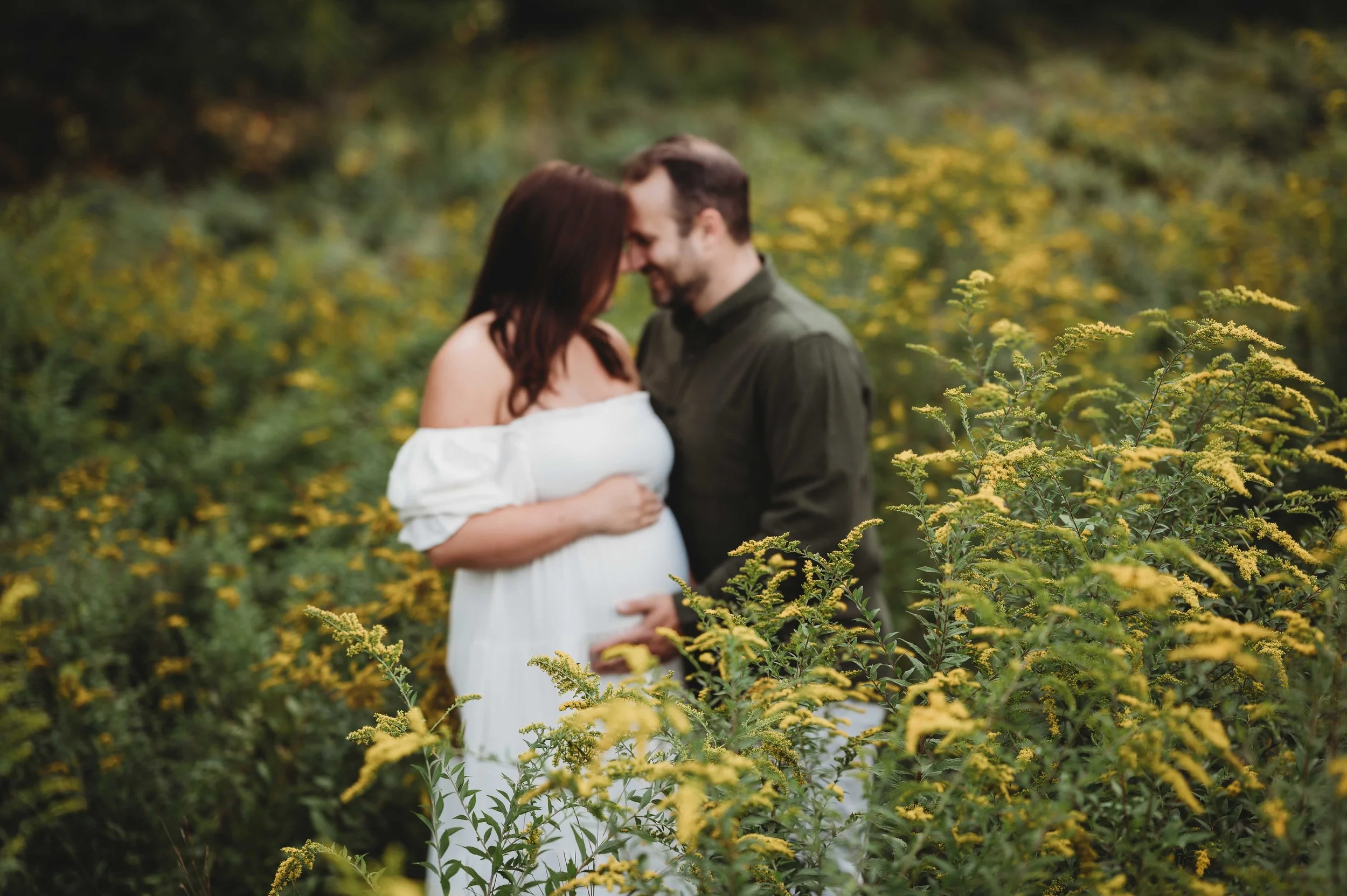 woman and husband snuggle in field of flowers, maternity photoshoot wilton