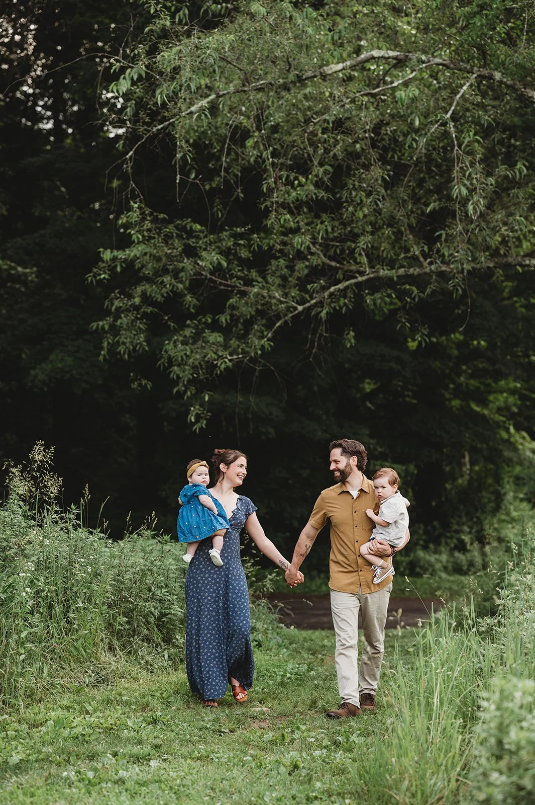 parents, each holding a young child, walk together in a field in Newtown, ct during a family photoshoot