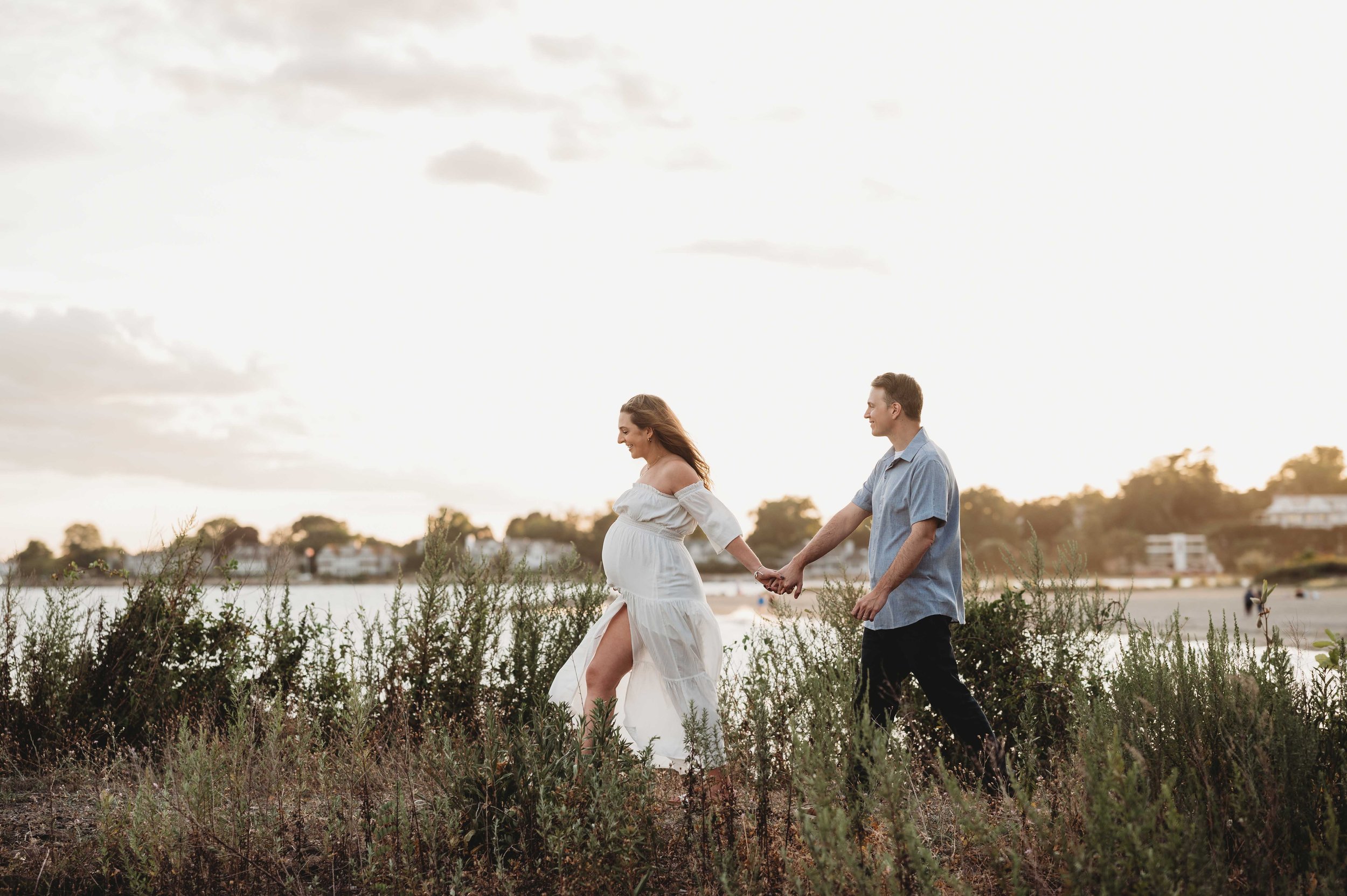 pregnant woman leads husband on a walk at the beach during a maternity photoshoot, Westport, ct