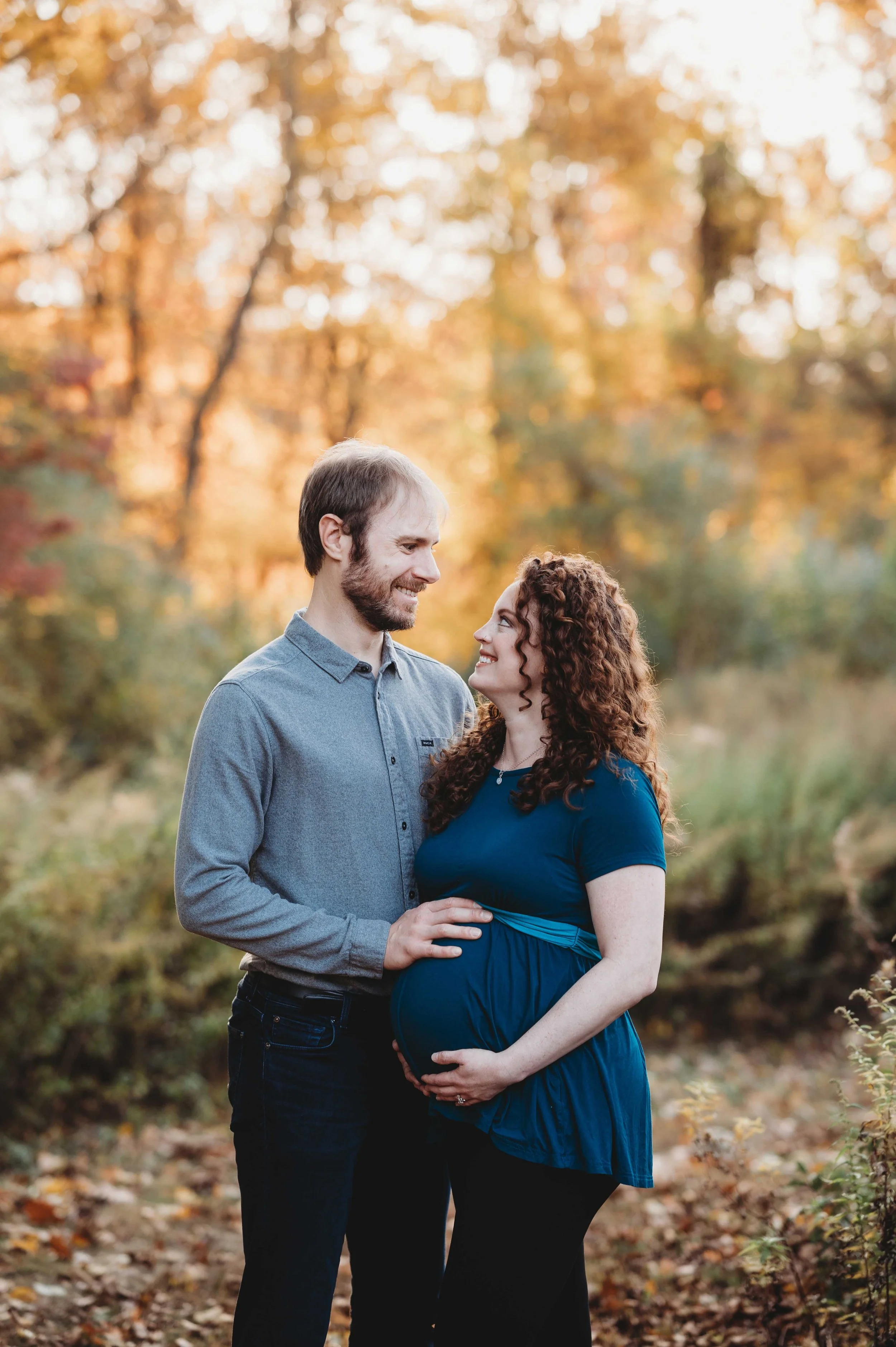 couple at outdoor maternity photoshoot wears casual clothes, fall foliage backdrop