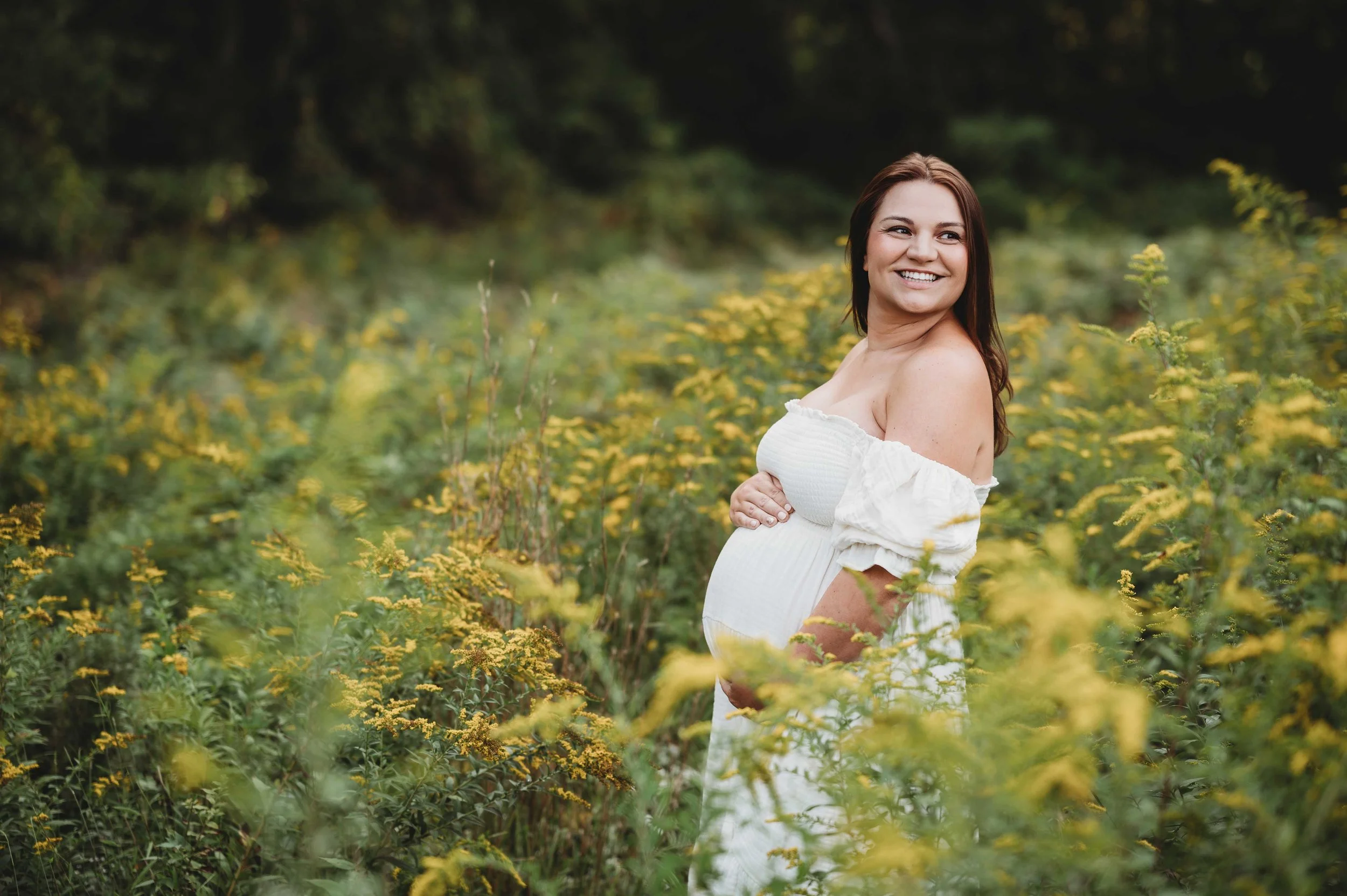 pregnant brunette woman stands in field surrounded by yellow flowers, wilton, ct maternity photography session