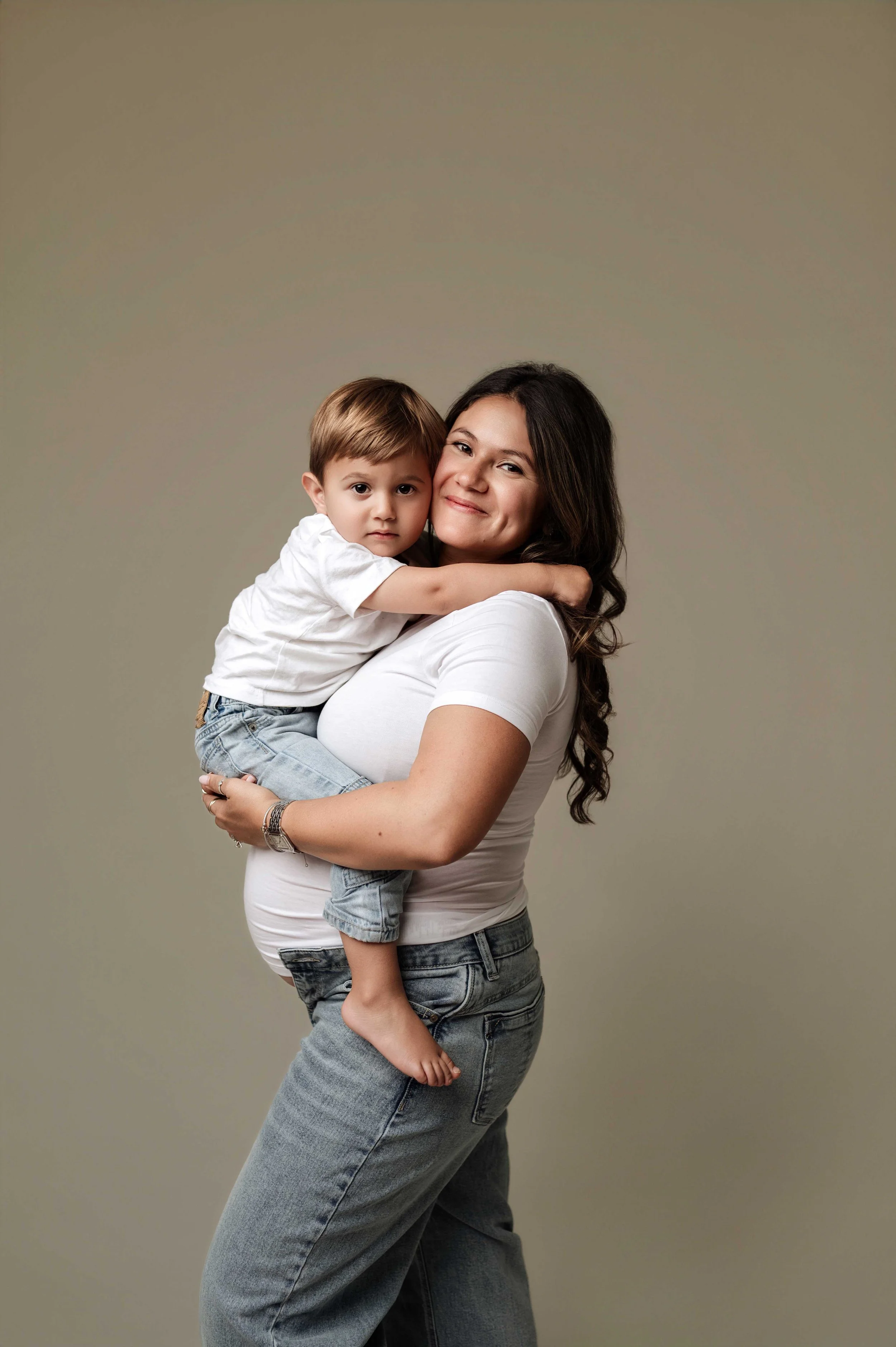 pregnant woman in white shirt holds toddler son during a studio maternity photoshoot, ridgefield, ct
