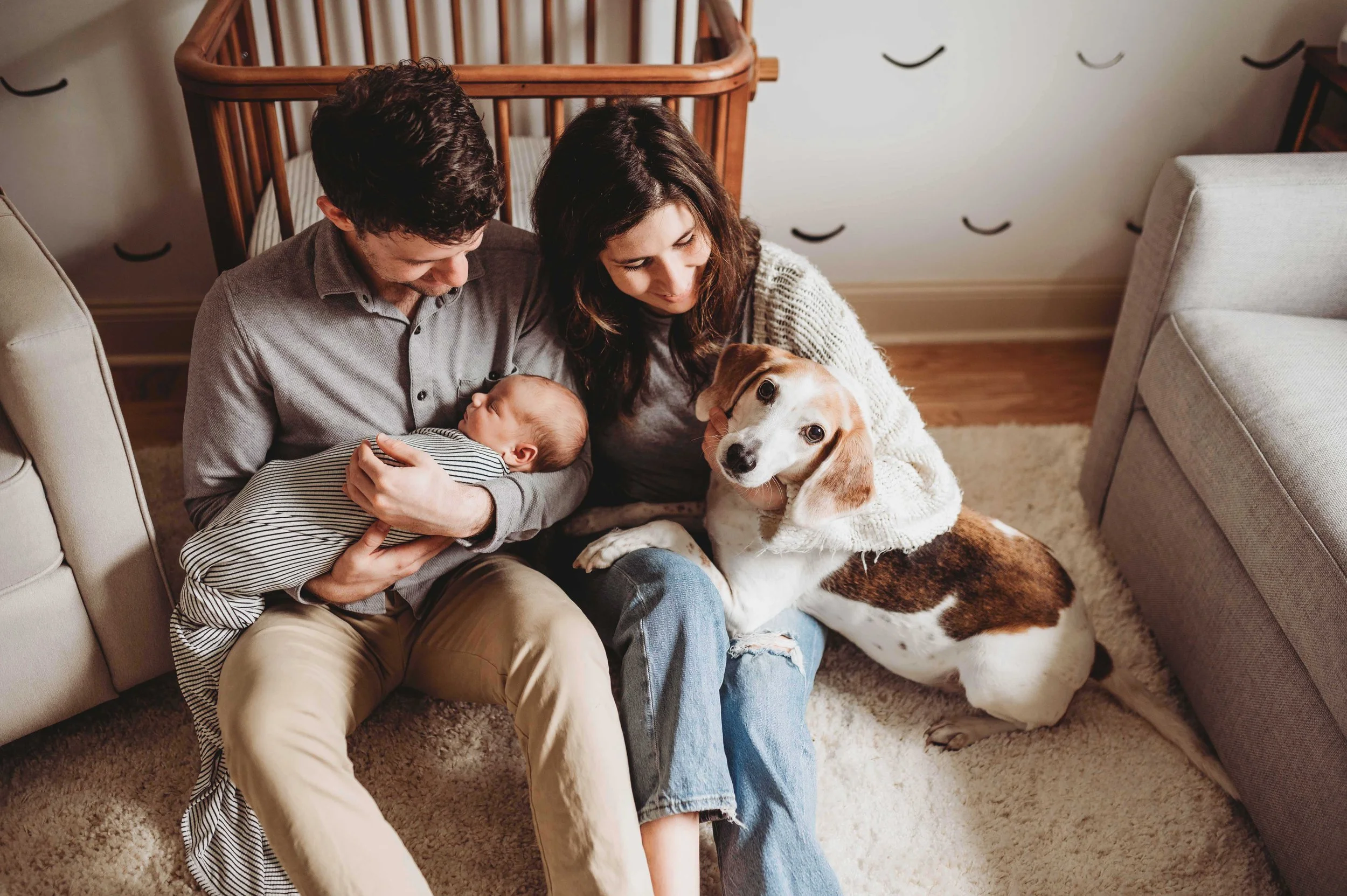 Fairfield County parents snuggle newborn baby and dog while sitting on the floor of their nursery in a lifestyle newborn photoshoot