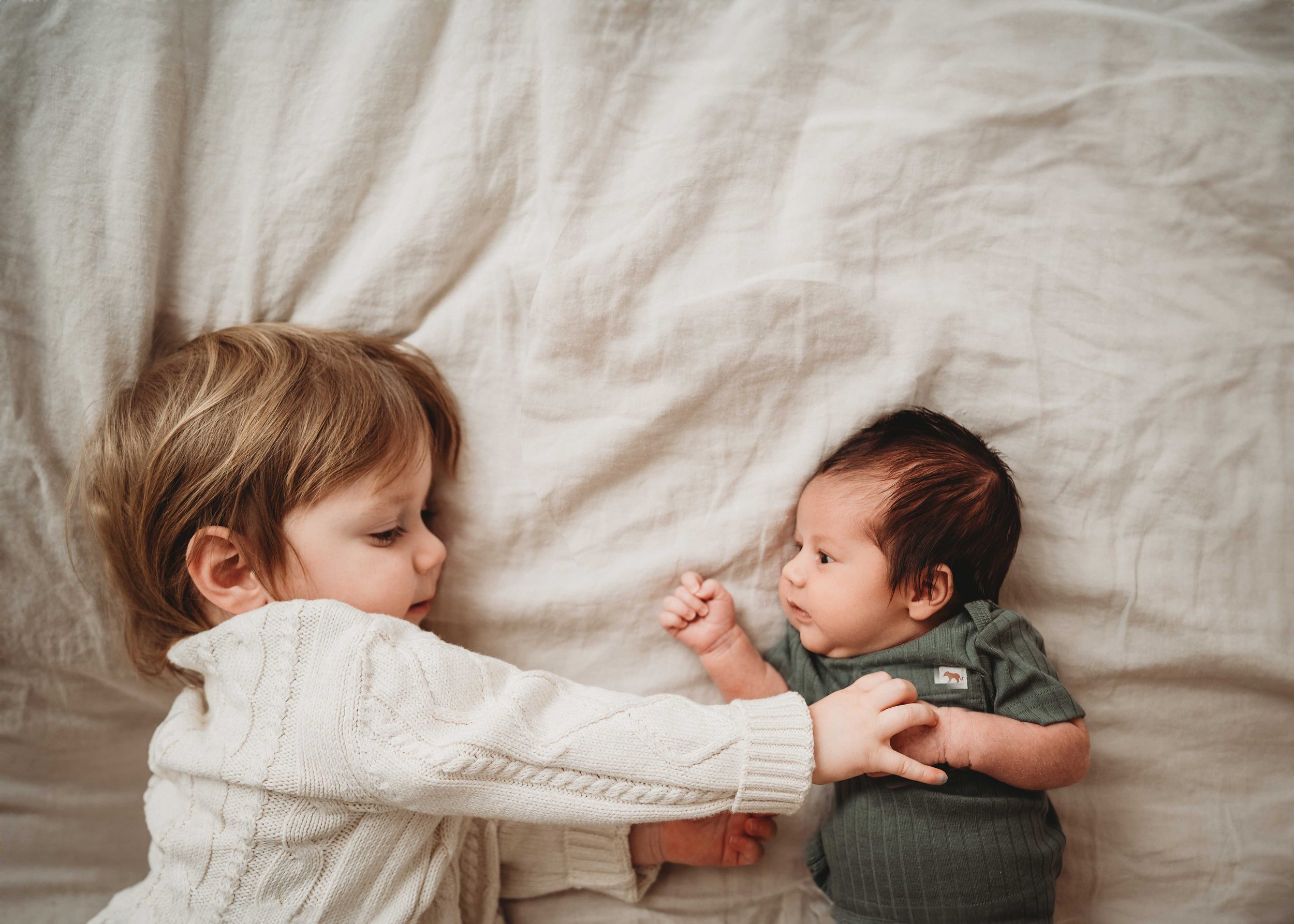 Newborn and sibling brother face each other on bed, Fairfield County CT newborn photography session in client's home