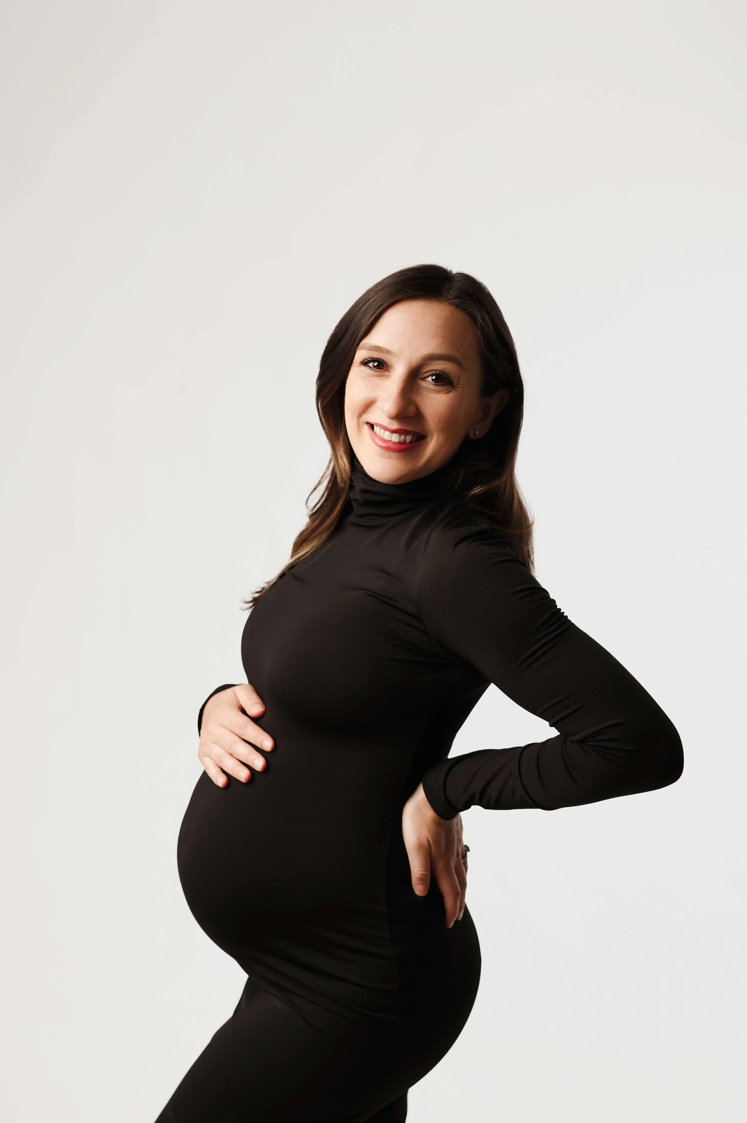 woman in black dress poses for a maternity photoshoot
