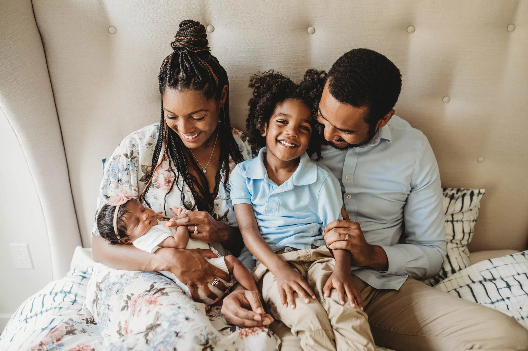 African American family of 4 snuggles on bed with two kids during Westchester newborn photoshoot