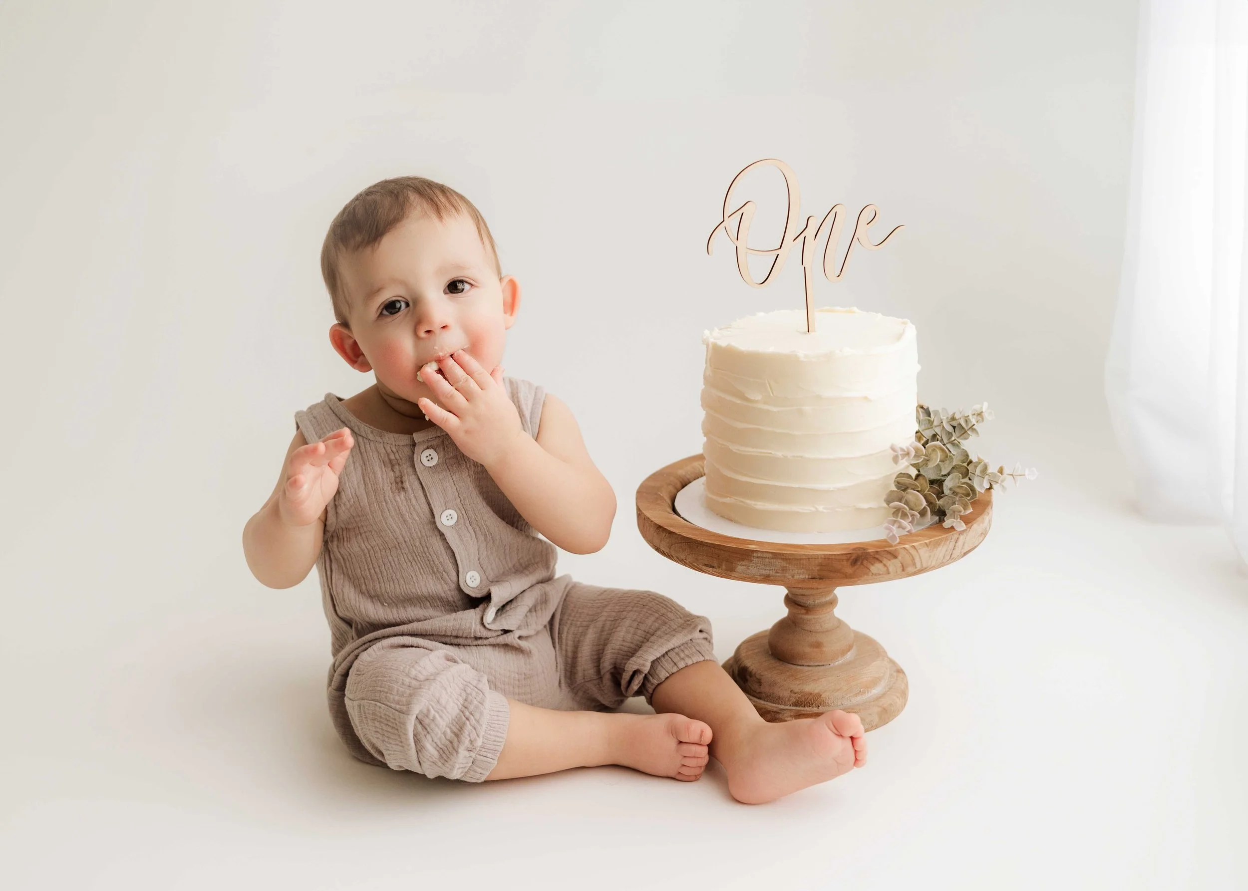 little boy sits on white floor and eats cake