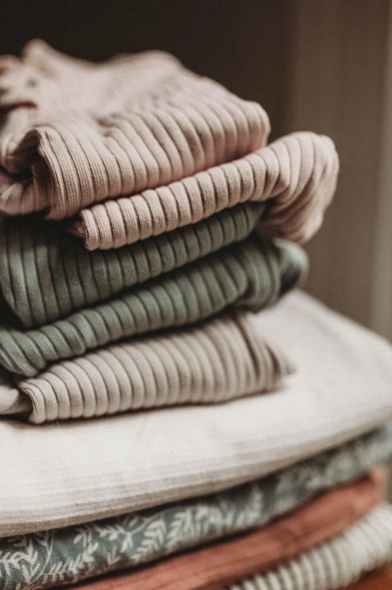 stack of newborn outfits and blankets in muted colors