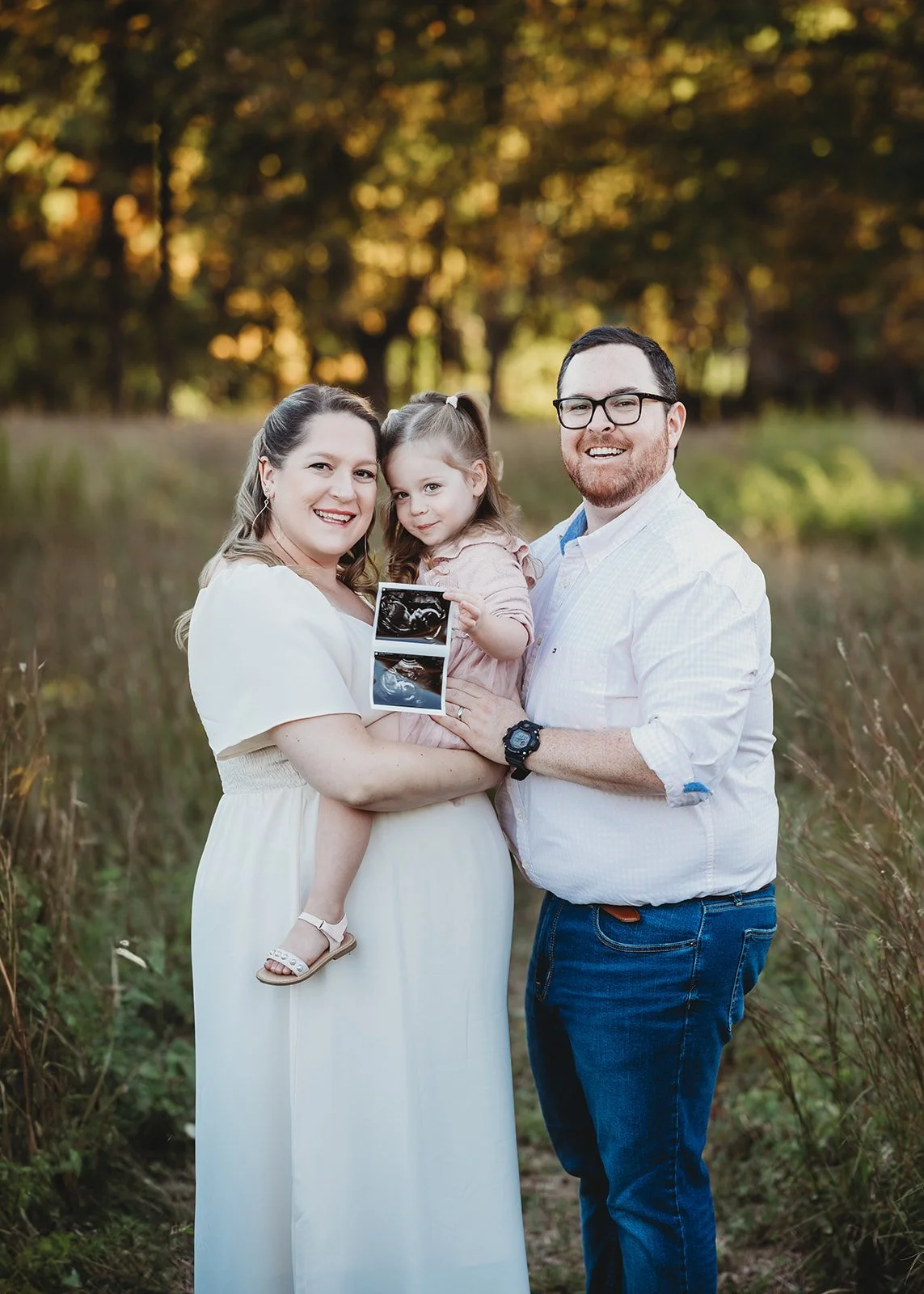 pregnant woman holds toddler with husband, holds ultrasound picture