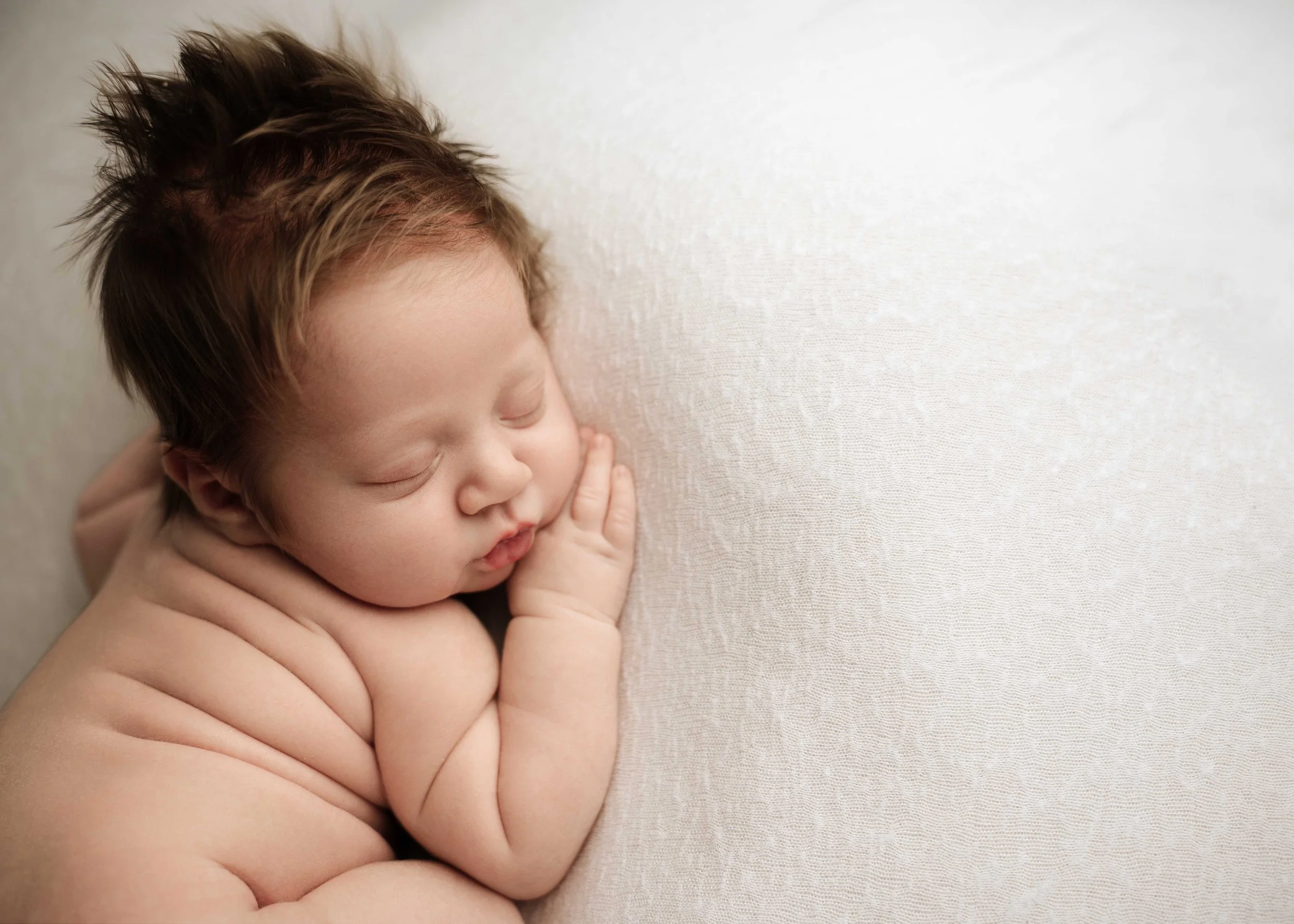 baby boy with lots of hair lays on his tummy with lots of back rolls