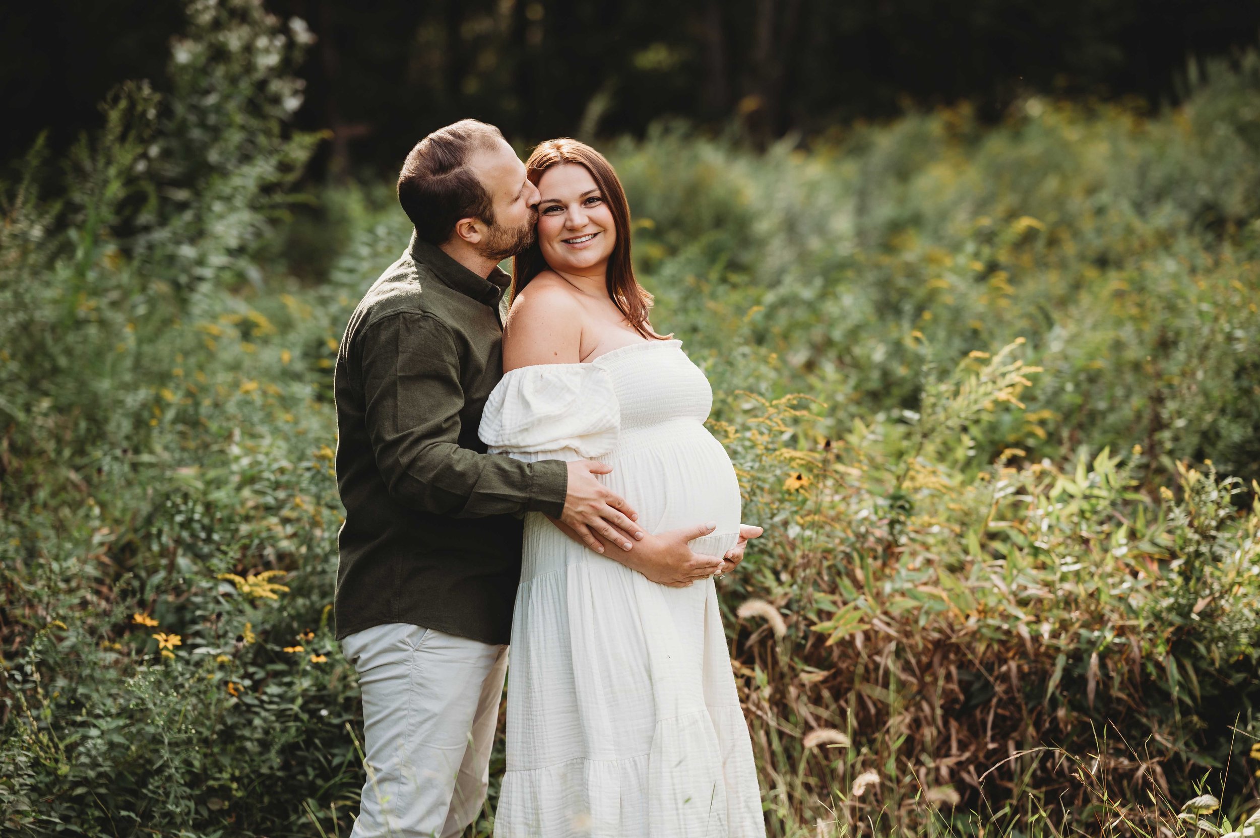 man and pregnant wife embrace in field of daisies, wilton ct