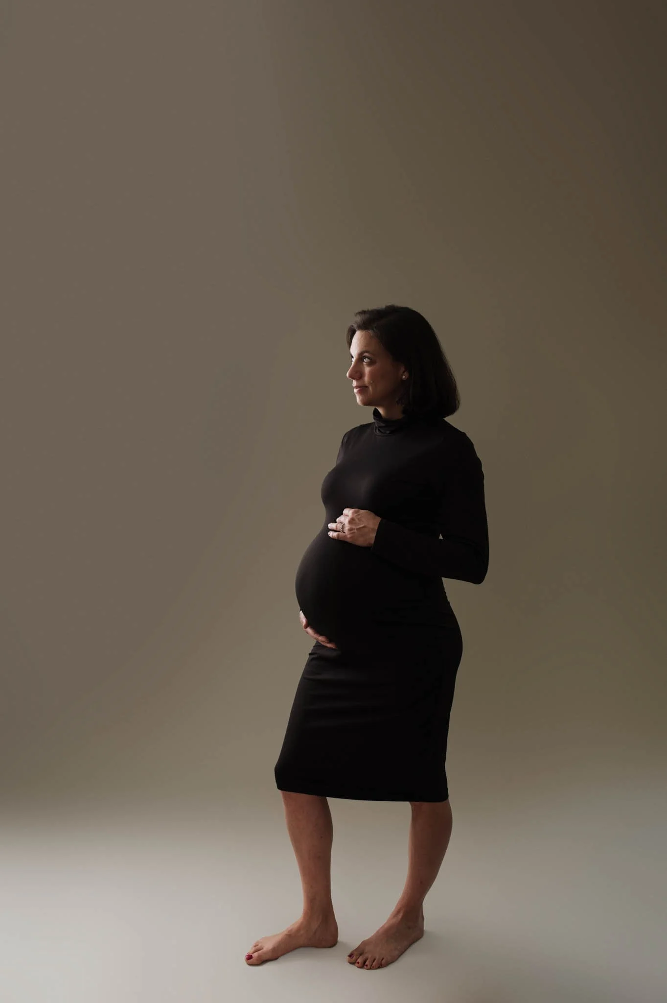 woman in black dress cradles bump, dramatic lighting