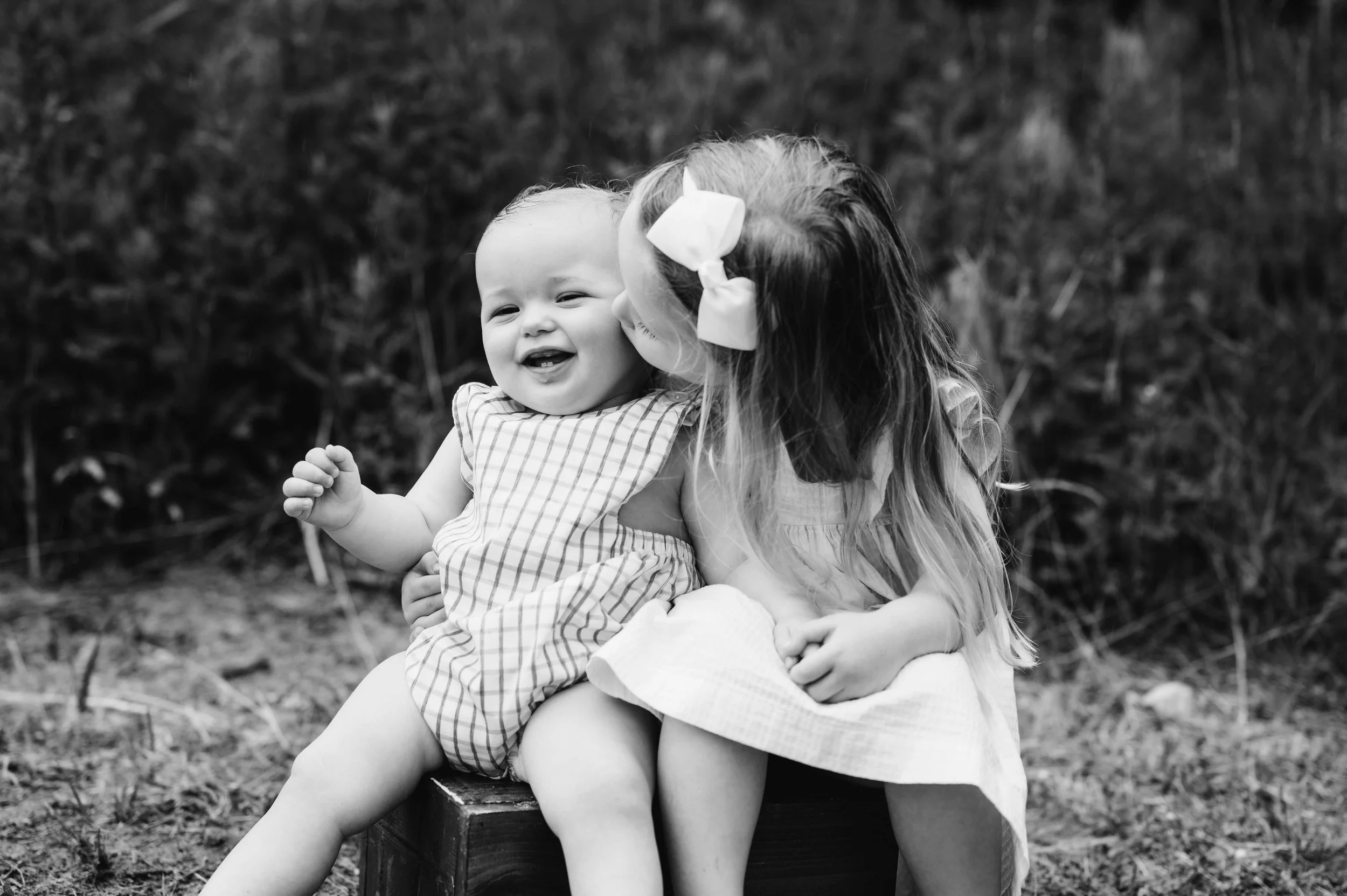 a toddler sister kisses baby brother on the cheek in a black and white photo, westport, ct beach location