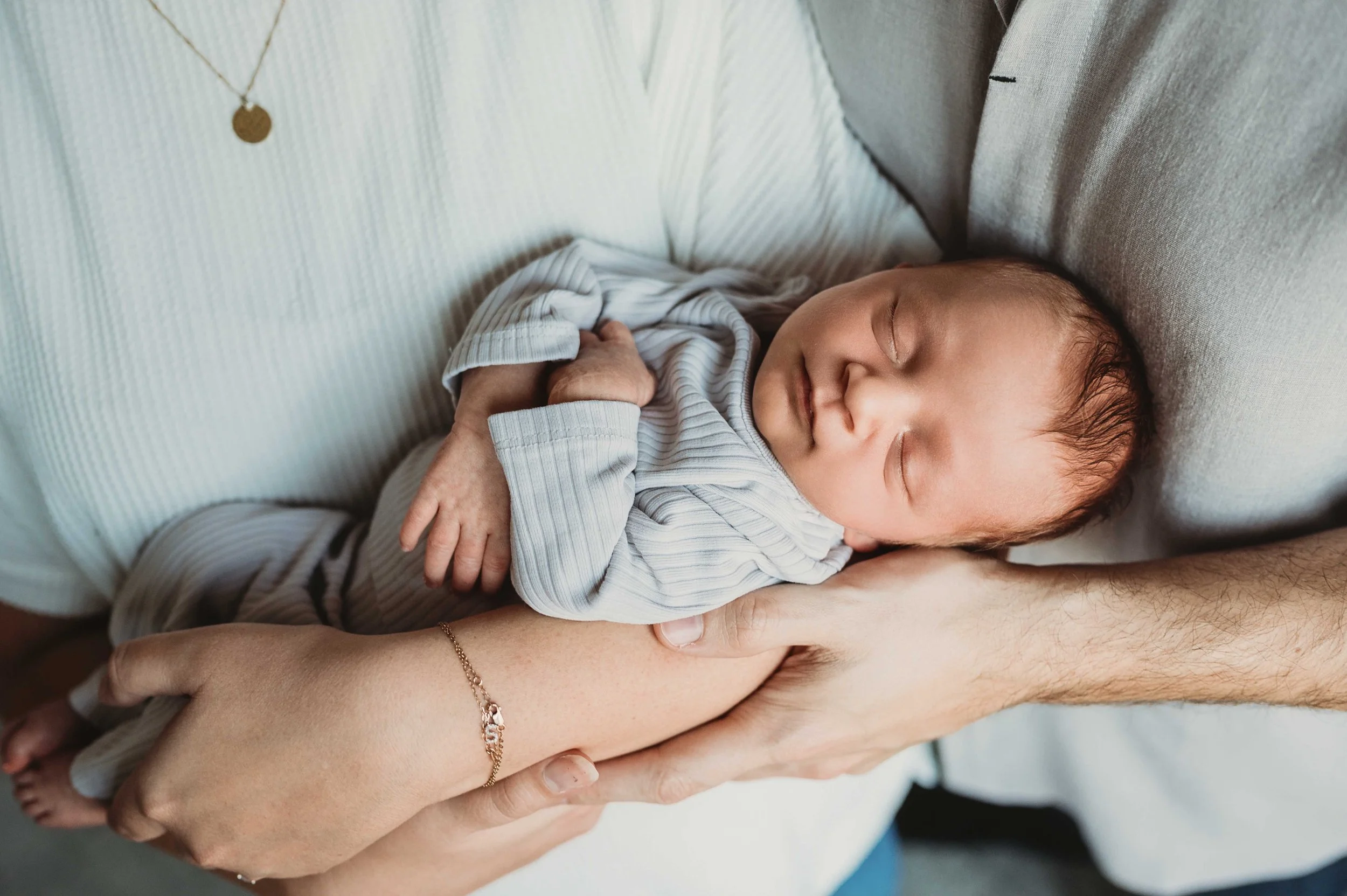 baby baby sleeps in parents' arms during an in-home newborn photoshoot in danbury, ct
