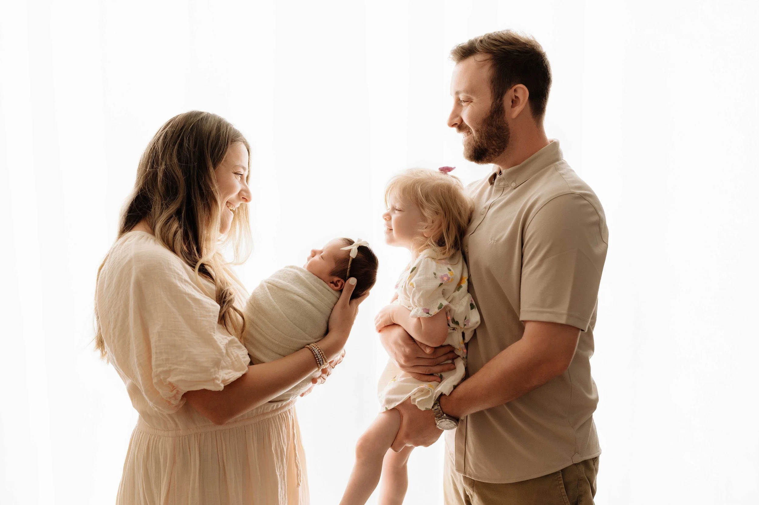 mom holding baby girl faces dad who is holding toddler daughter against a white backdrop in a ridgefield, ct studio
