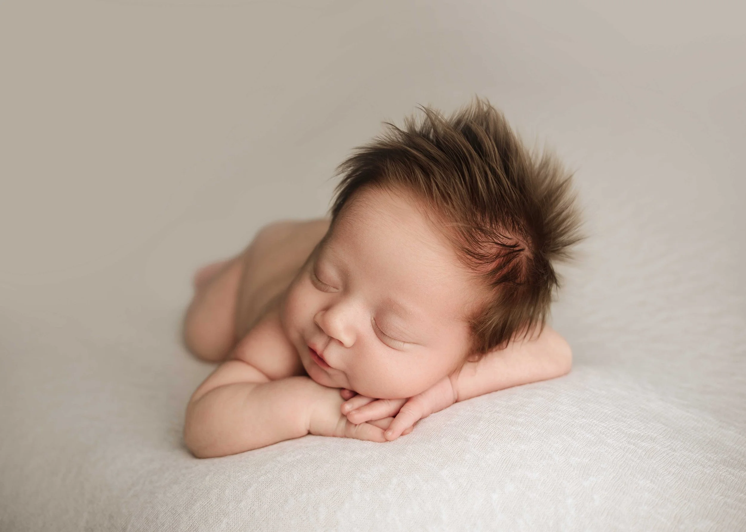 baby boy lies facing camera on tummy on a cream blanket