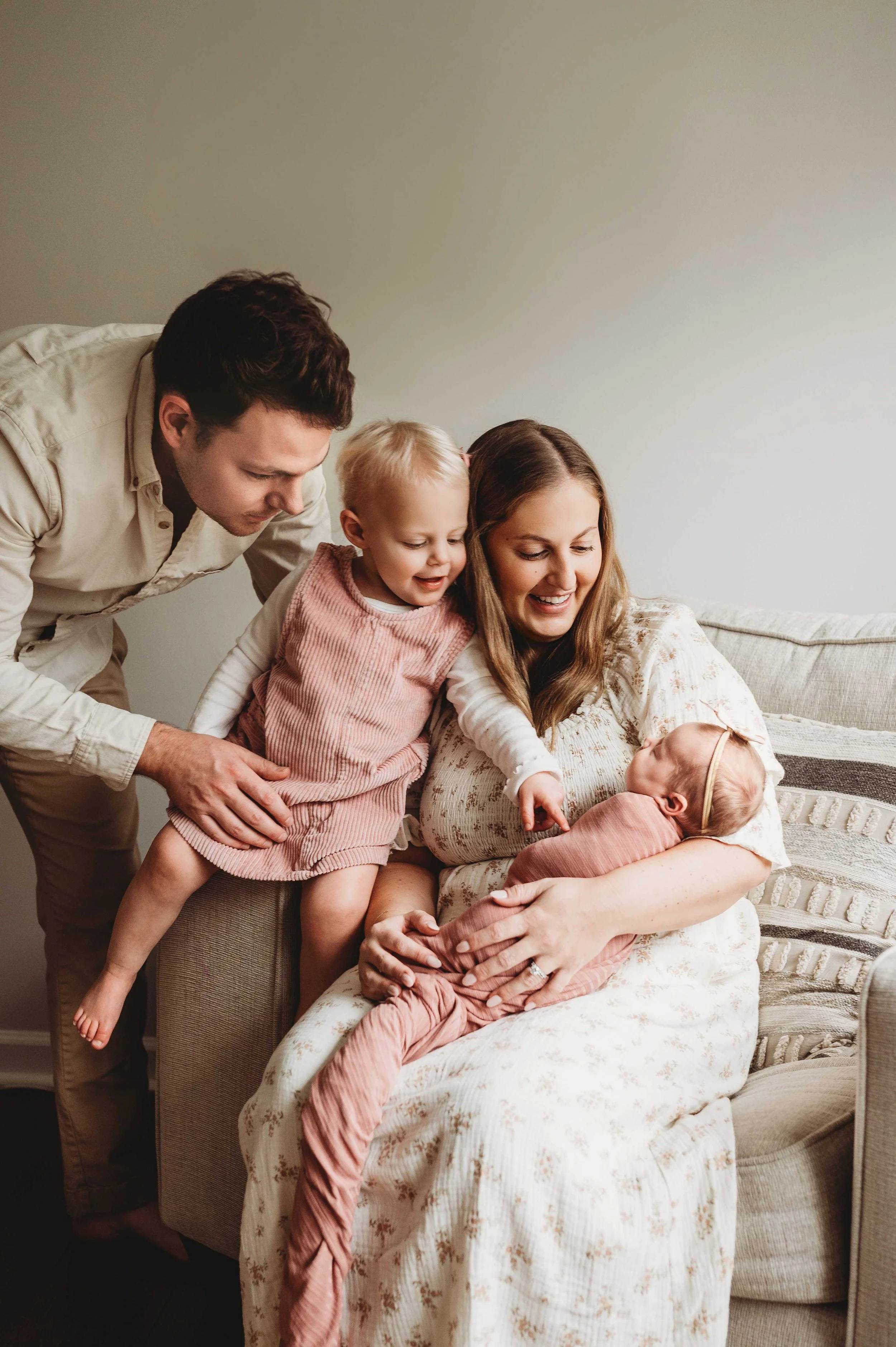 mom at in-home Lifestyle newborn photography session holds baby and dad and sibling look on in Fairfield County, ct