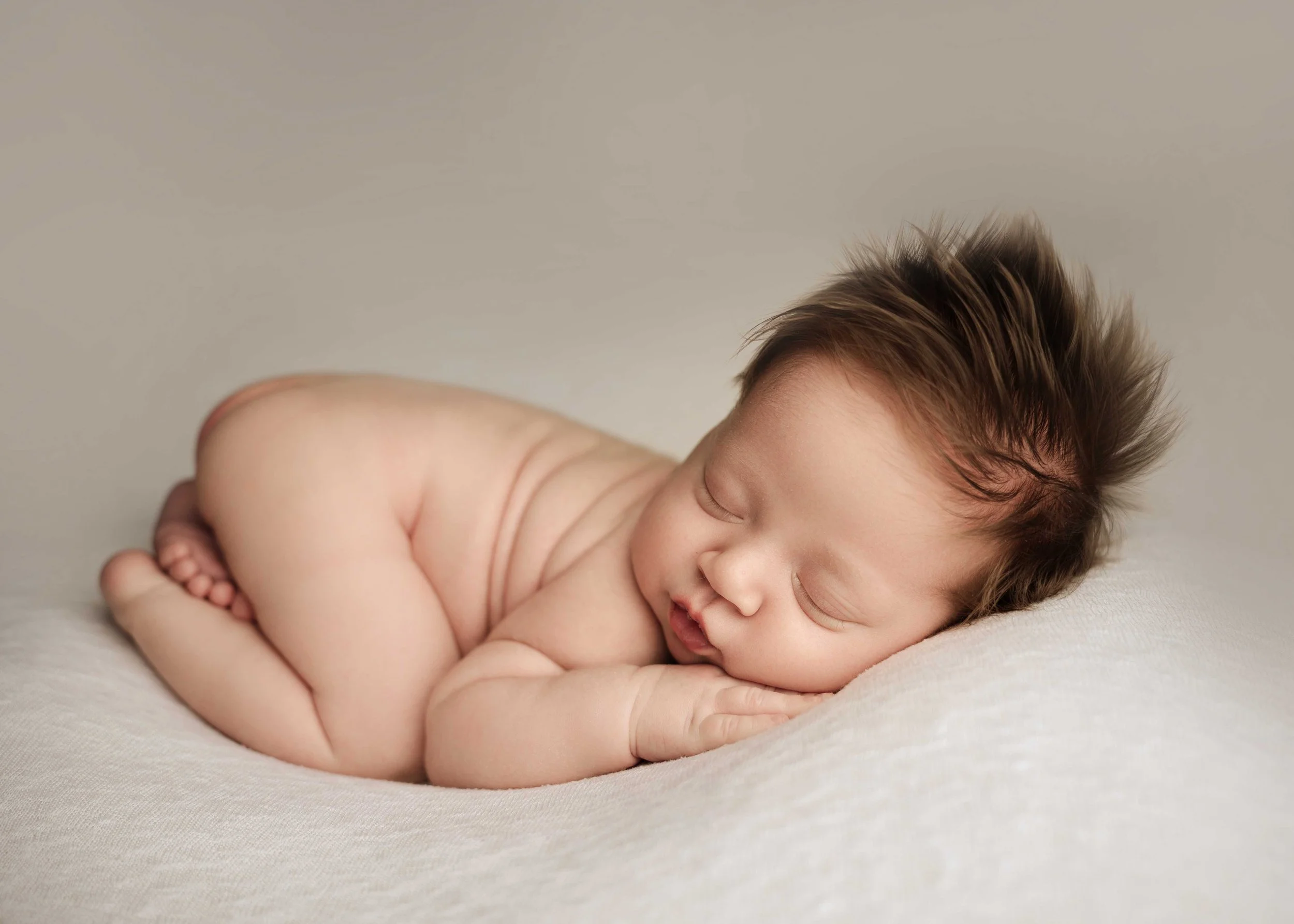 baby boy lies in "bum up" pose on cream blanket