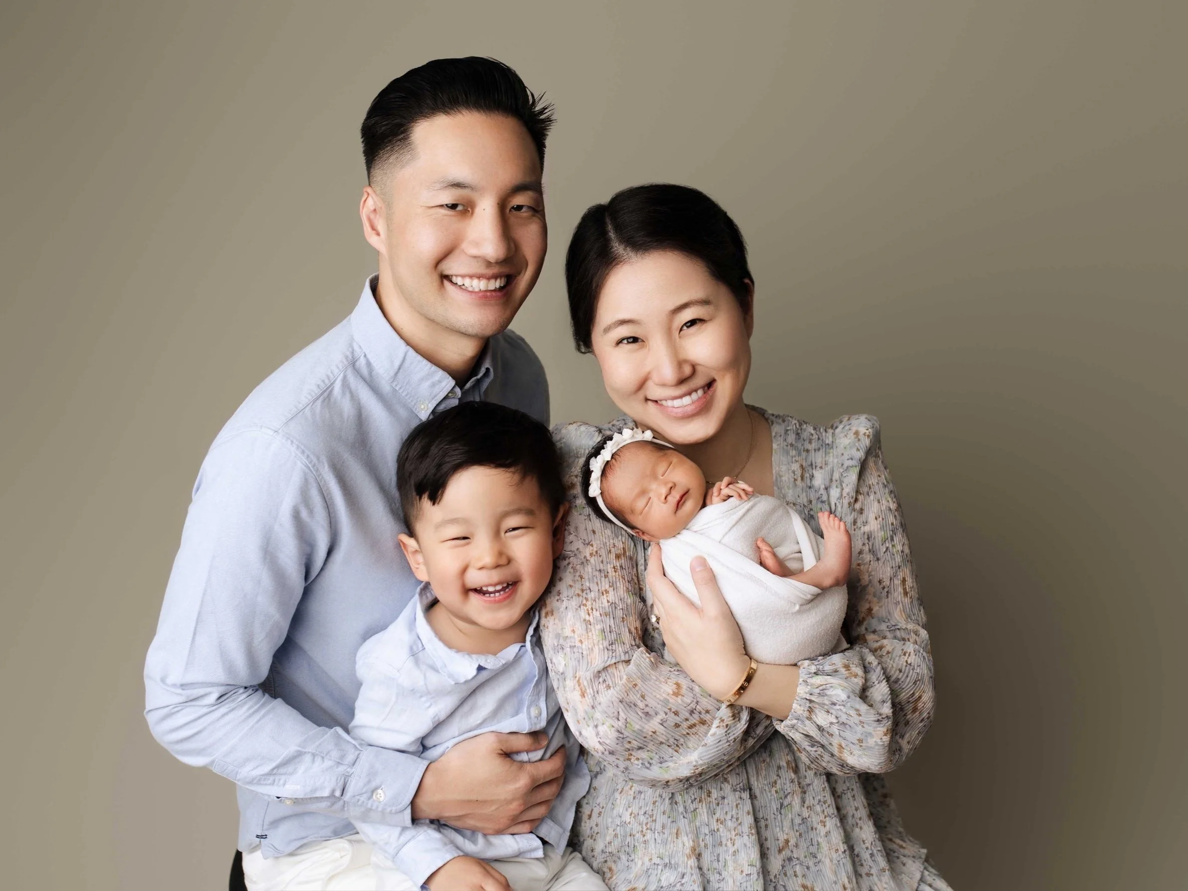family of four poses against a tan backdrop. includes dad, mom, toddler son, baby girl