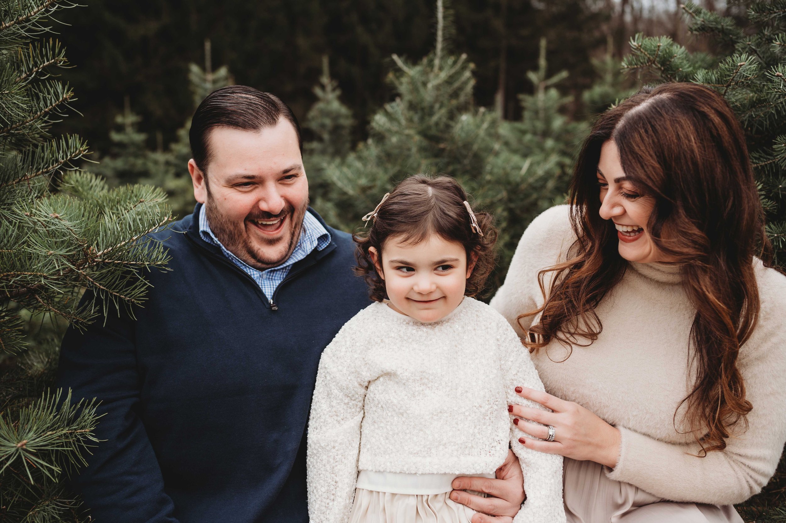 two parents look at daughter sitting between them, laughing at her expression