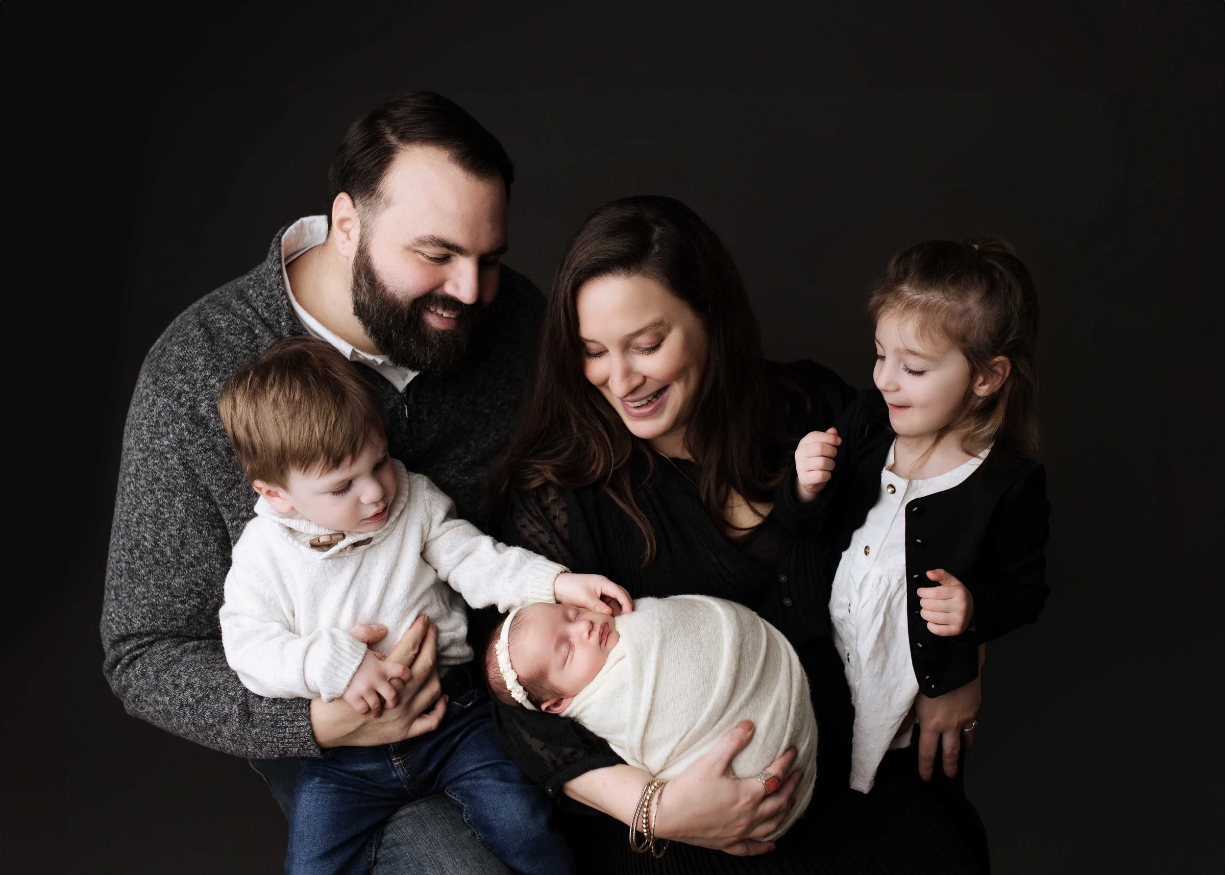 Family of five with two toddlers and a newborn baby posing together against a gray backdrop during a professional studio photography session in Fairfield County, CT.