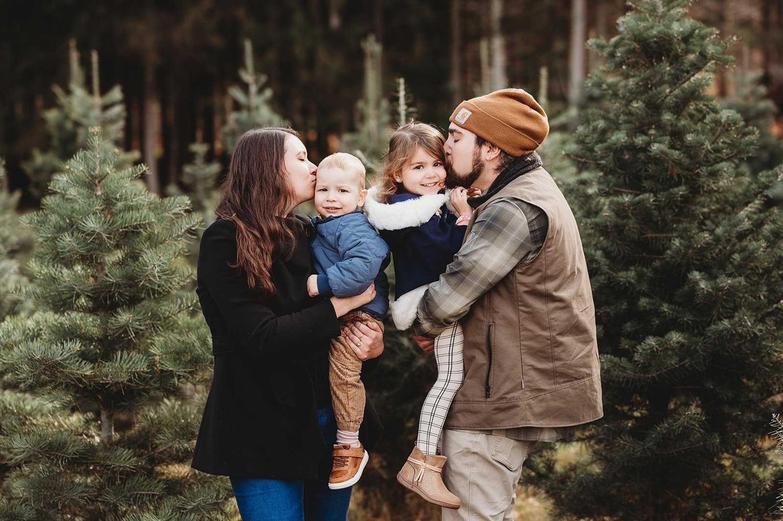 parents stand in christmas tree farm in Bethel, ct, holding their two children