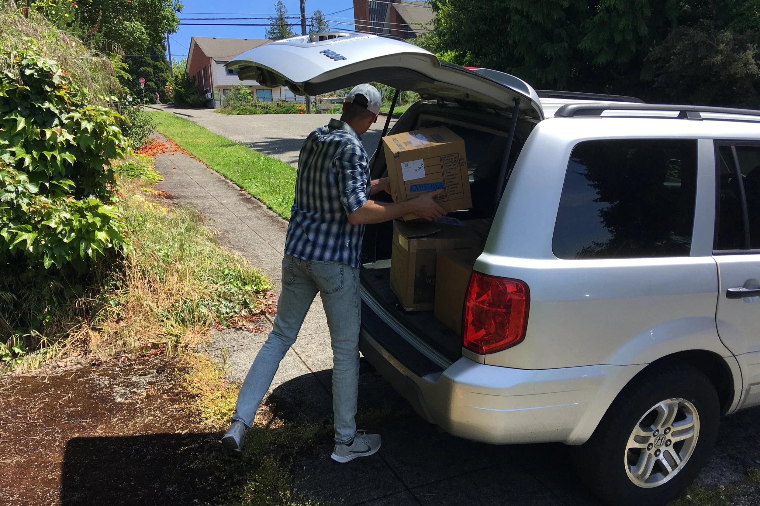 A man loading cardboard boxes into the open trunk of a silver SUV.