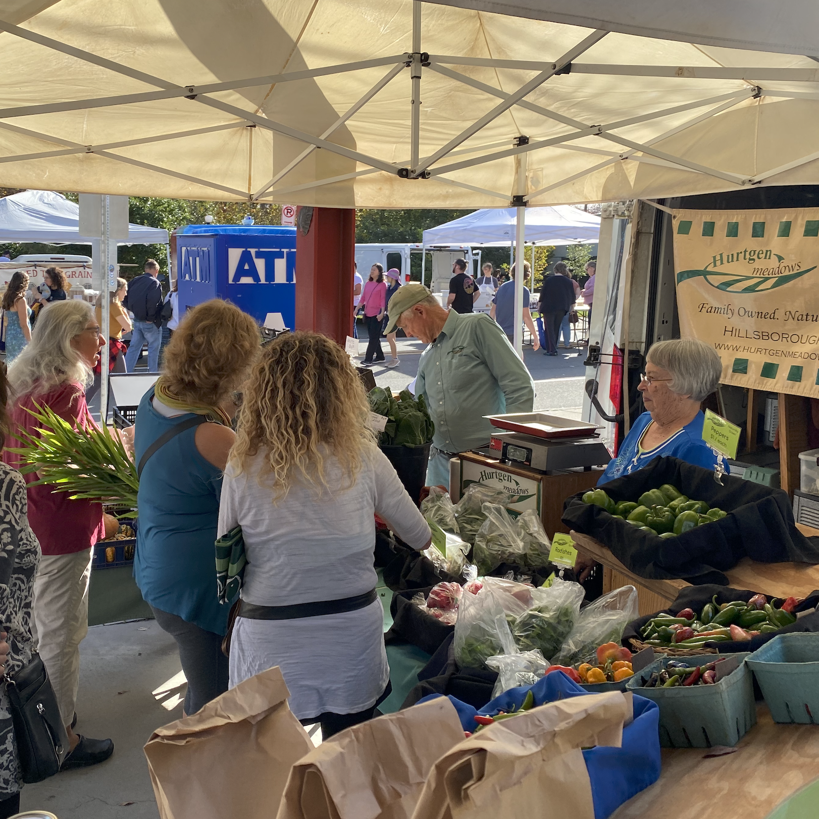 A local farmers marketing booth with a table full of farm fresh products and farmers selling them.