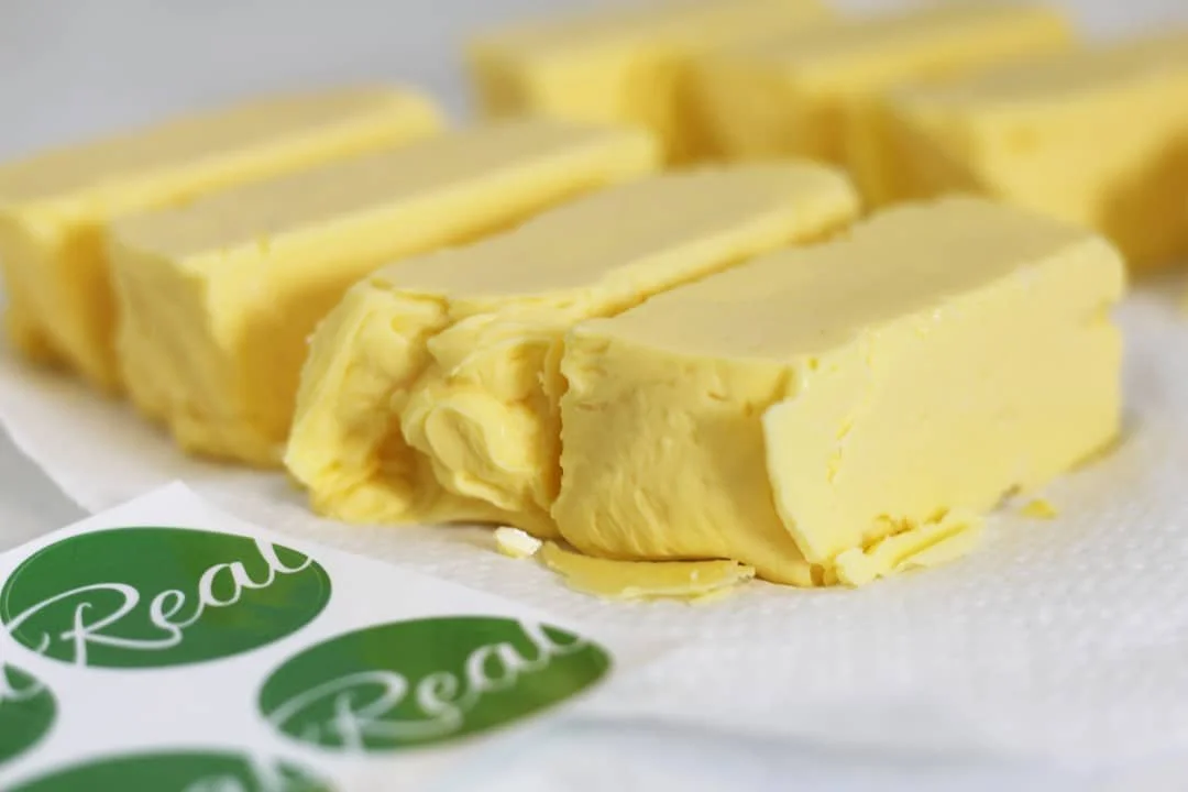 Several sticks of yellow butter on parchment paper with green labels, arranged in rows.
