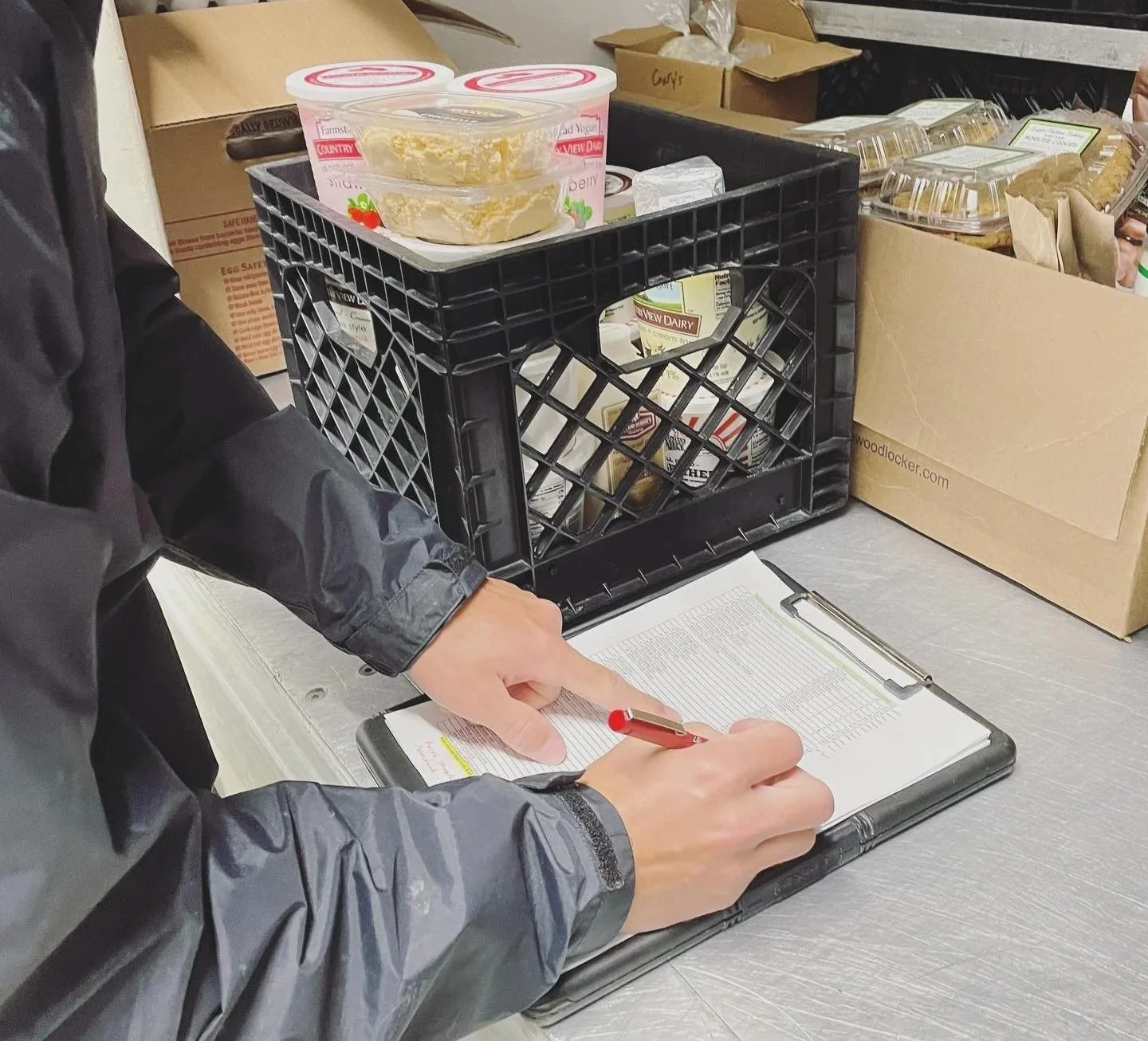 Person checking a clipboard delivery list beside crates filled with dairy products and baked goods.