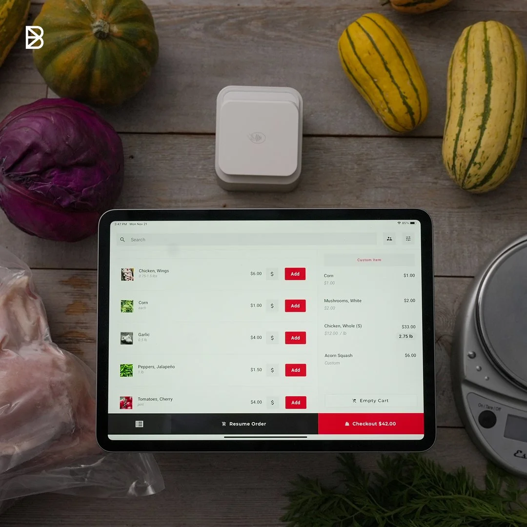 The Barn2Door POS device and app on an iPad with produce and farm products in the background.