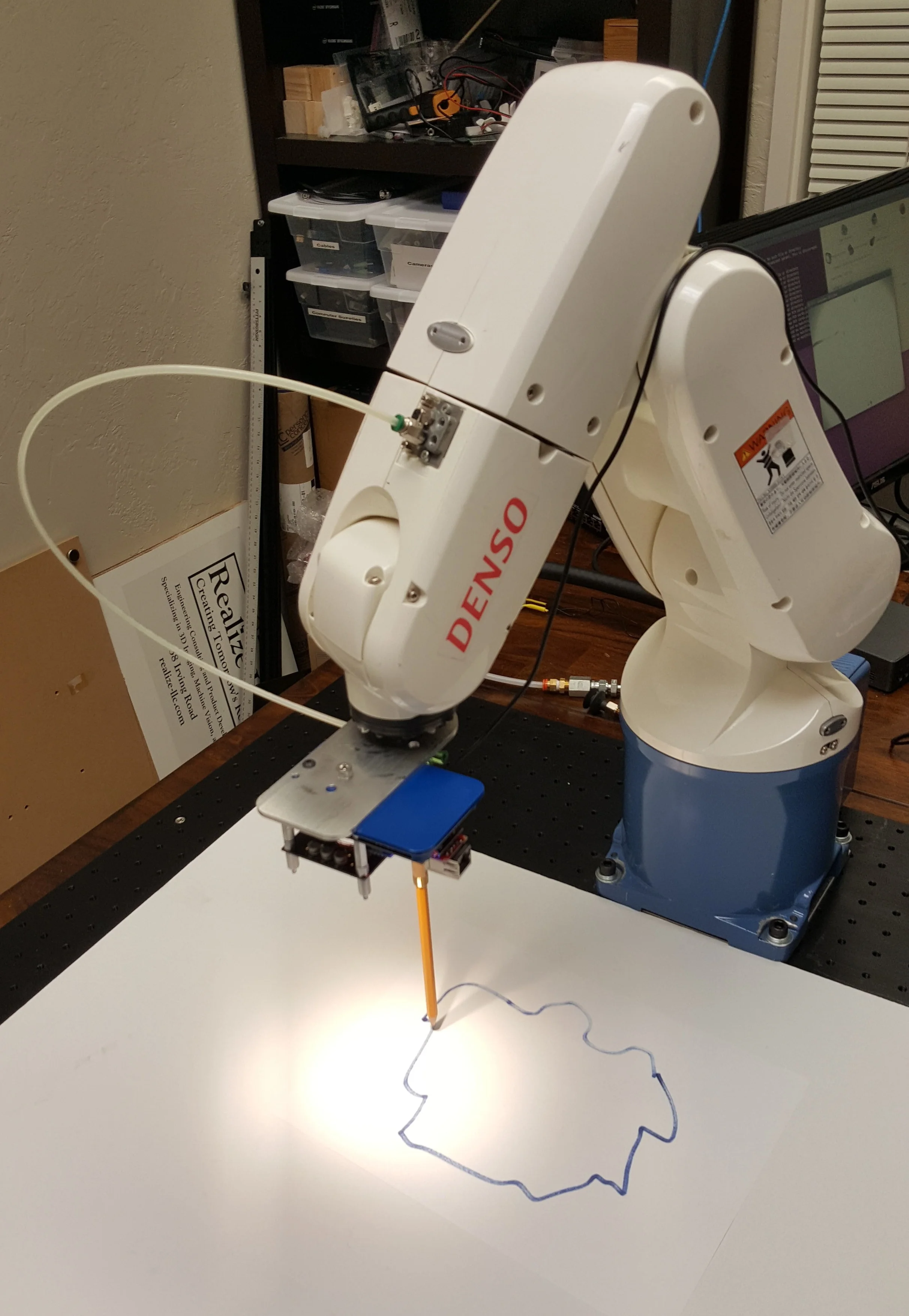 Following a Line There are many applications that require following a templated line or pattern in order to cut a shape out of a piece of material. Rigid materials such as steel are fairly straightforward for traditional robots to follow a pattern. But what happens if the material is flexible like rubber , fabric , or plastic ? What if it moves or deforms while being cut? That would require a vision system that can maintain its course even when things move a bit, like our Vision-in-Motion technology can do. We're currently working on a research project for a large manufacturer facing exactly that problem. In this image we're investigating the tracing of an outline using a pencil as a stylus.