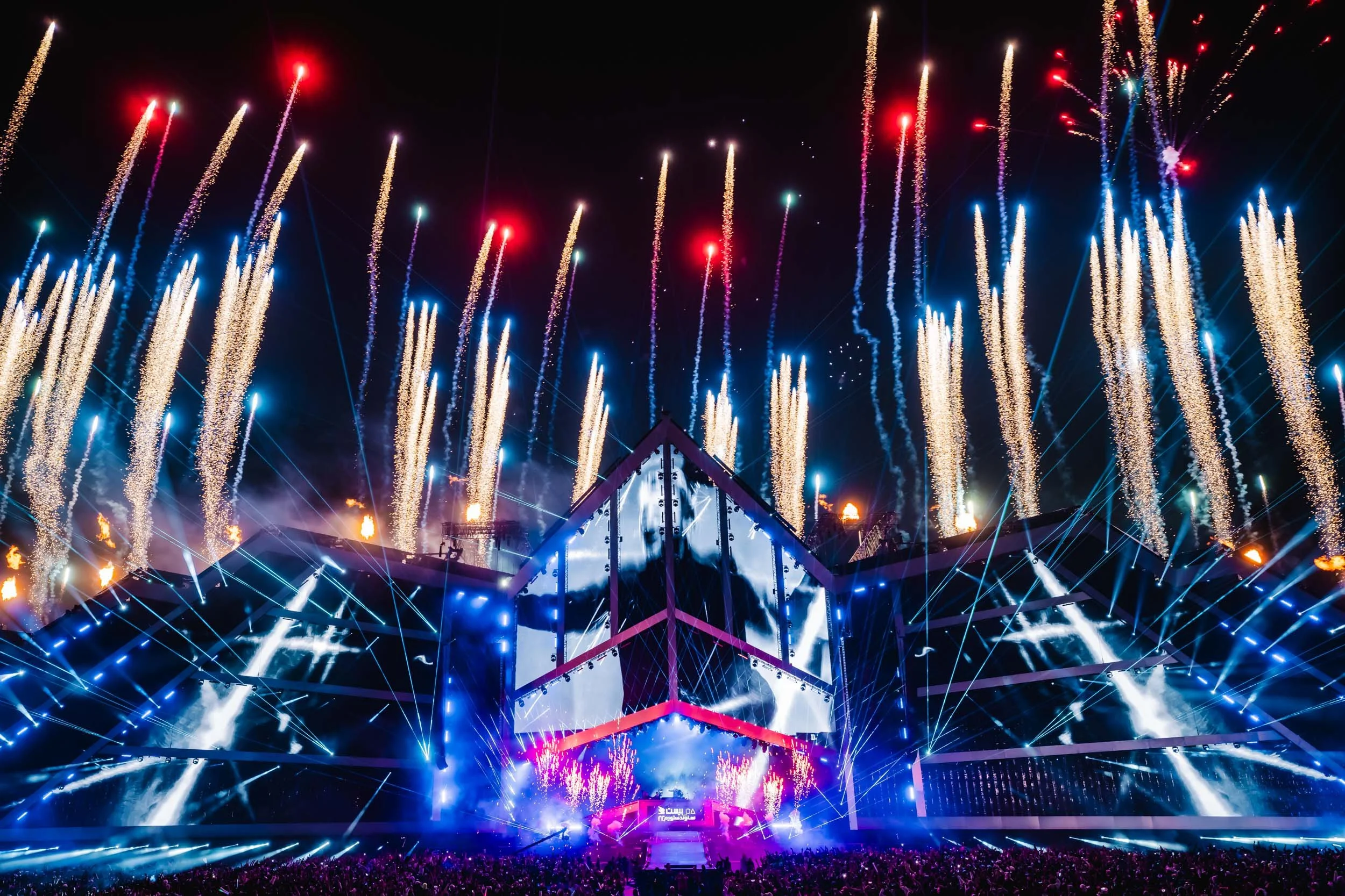 Professionelles Foto einer Festivalbühne, beleuchtet von synchronisierten Lasern und Feuerwerk.