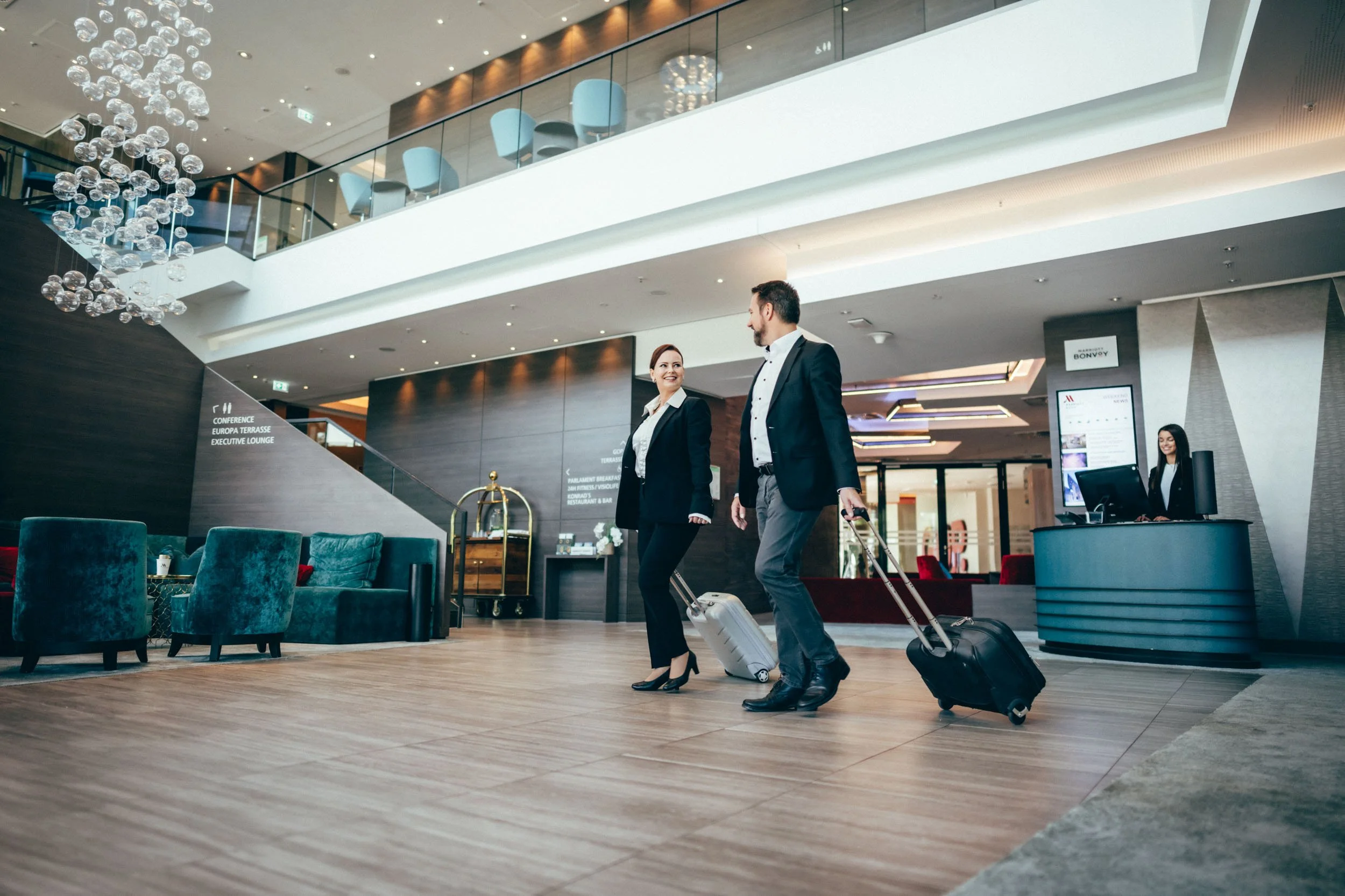Stimmungsvolle Fotografie eines Paares, das in der eleganten Hotel-Lobby ankommt – perfekt, um die gehobene Atmosphäre und den exklusiven Empfangsbereich des Hotels hervorzuheben.