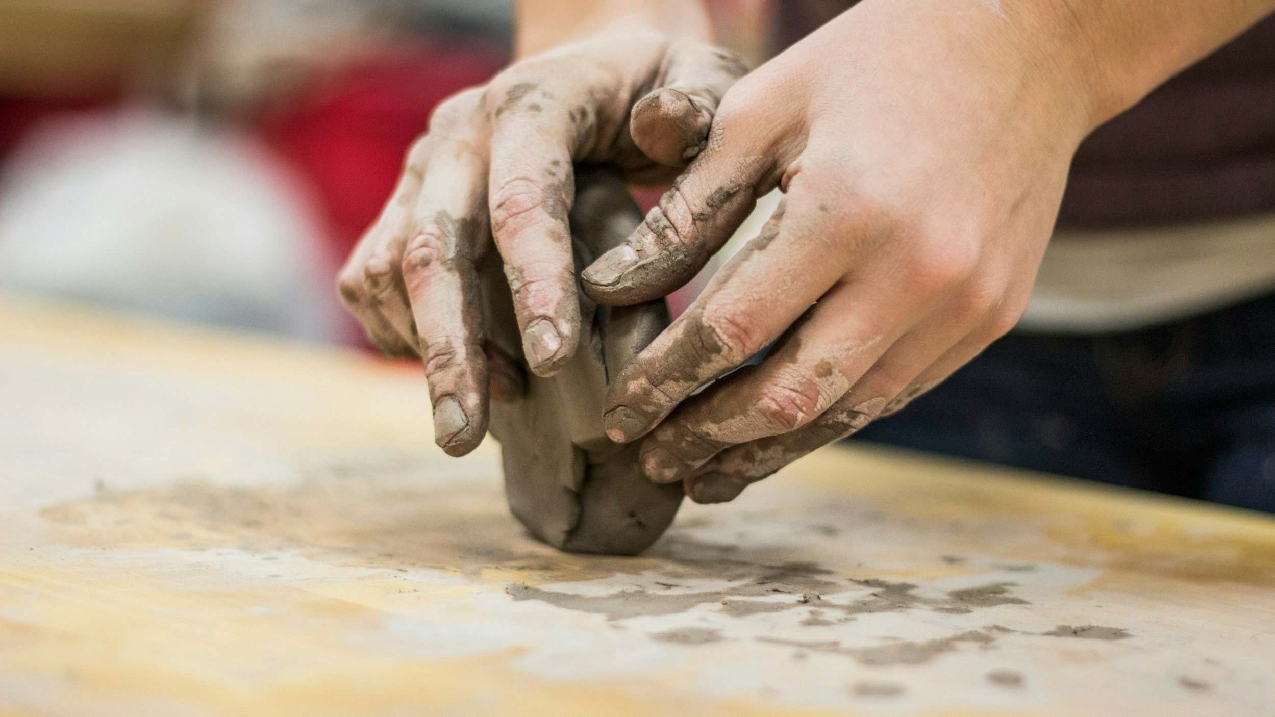 Close-up of hands shaping clay on a table, with one hand holding and the other smoothing the clay.
