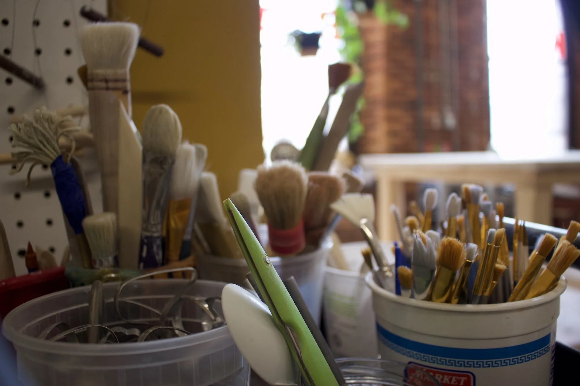 Various brushes, paint tools, and a pair of scissors in containers