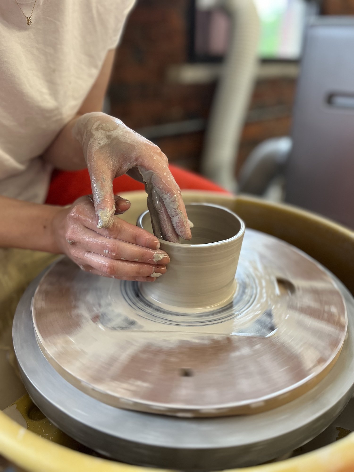 shaping a clay pot on a pottery wheel in a studio.
