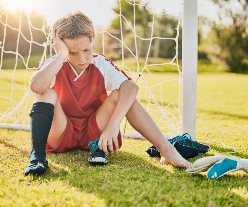 child in soccer uniform sitting on field with foot pain