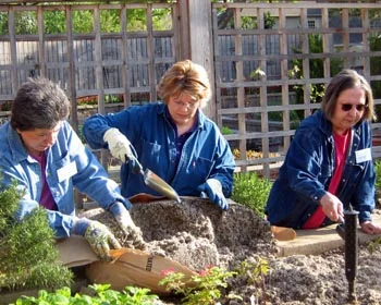 Mulch is used extensively to conserve water and act as soil enrichment. Linnaeus Gardeners add cotton hull mulch to a raised bed.