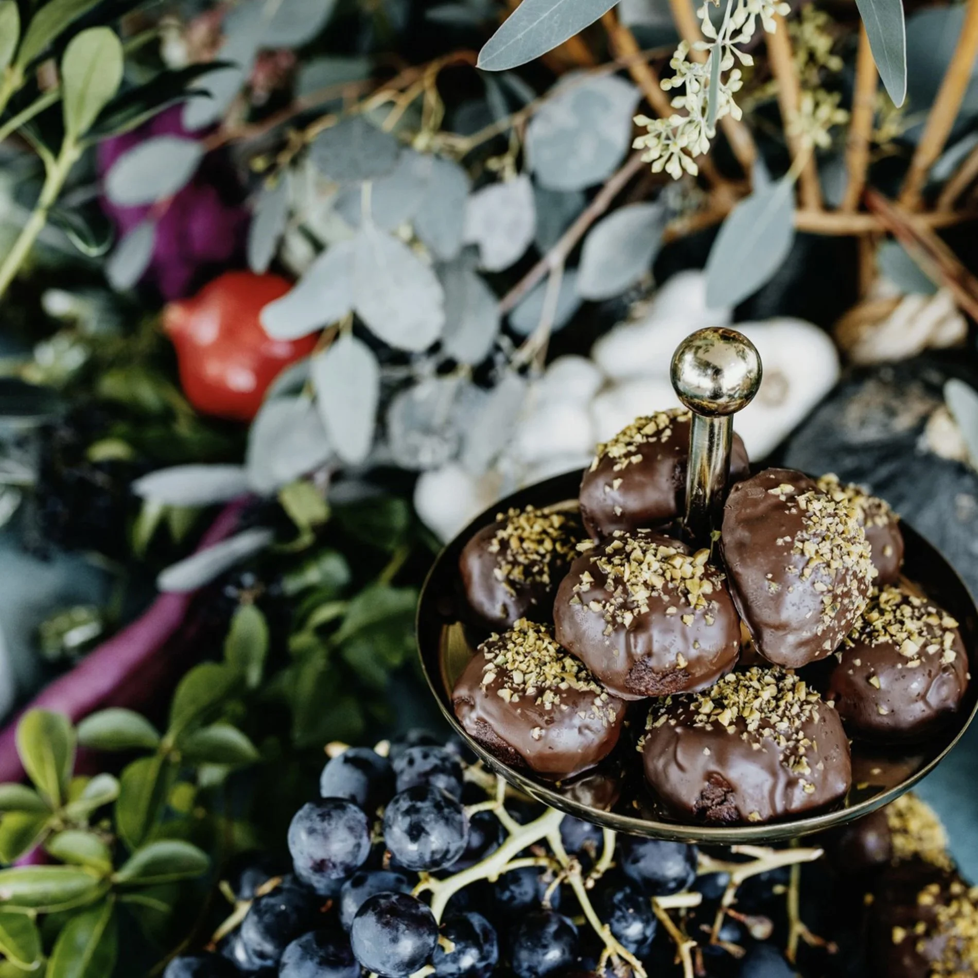 Schokoladenkuchenbällchen mit Nüssen auf einer Schmuckplatte, umgeben von Trauben, Blättern und Früchten.