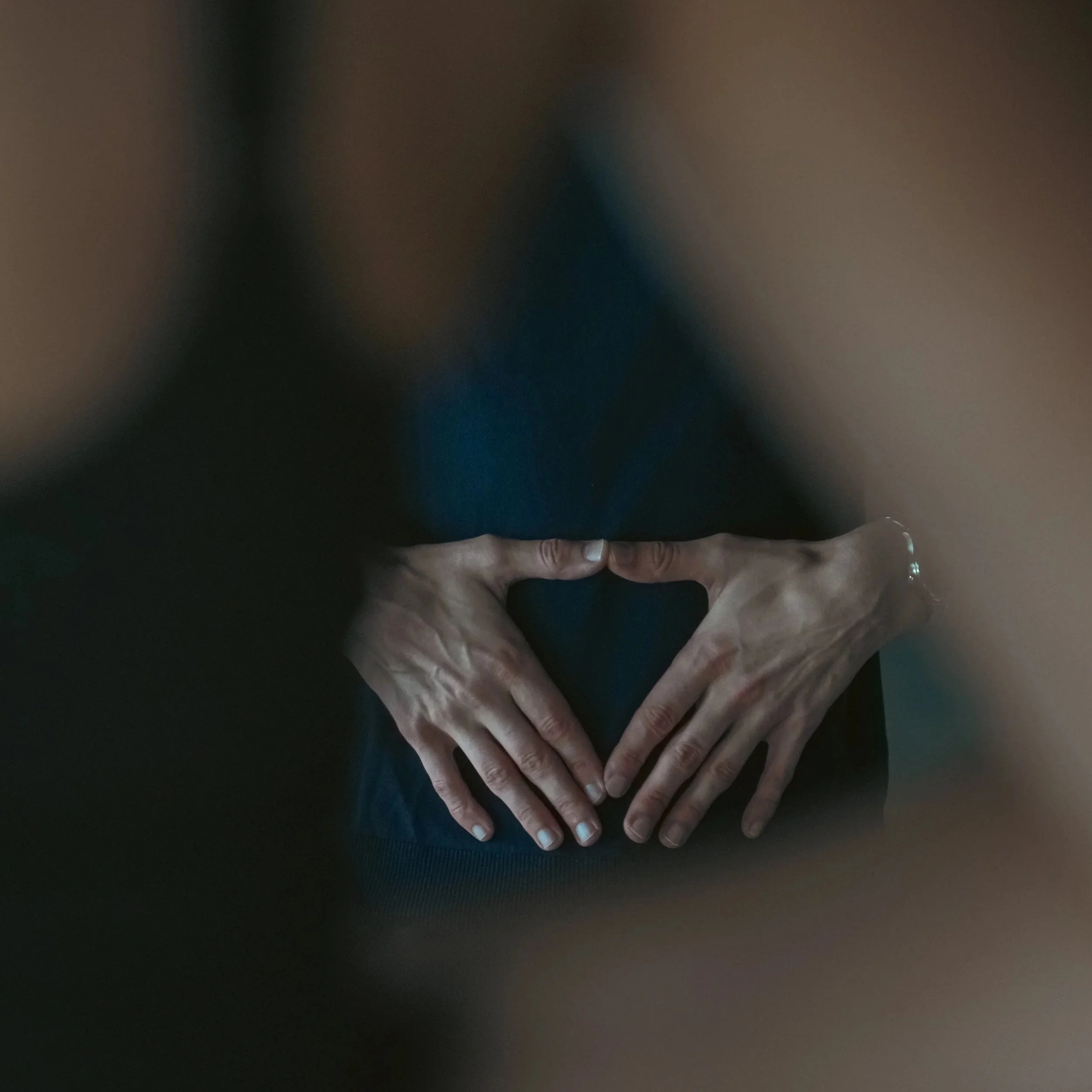 Nahaufnahme von Händen, die ein Herz formen, vor einem dunklen Hintergrund.