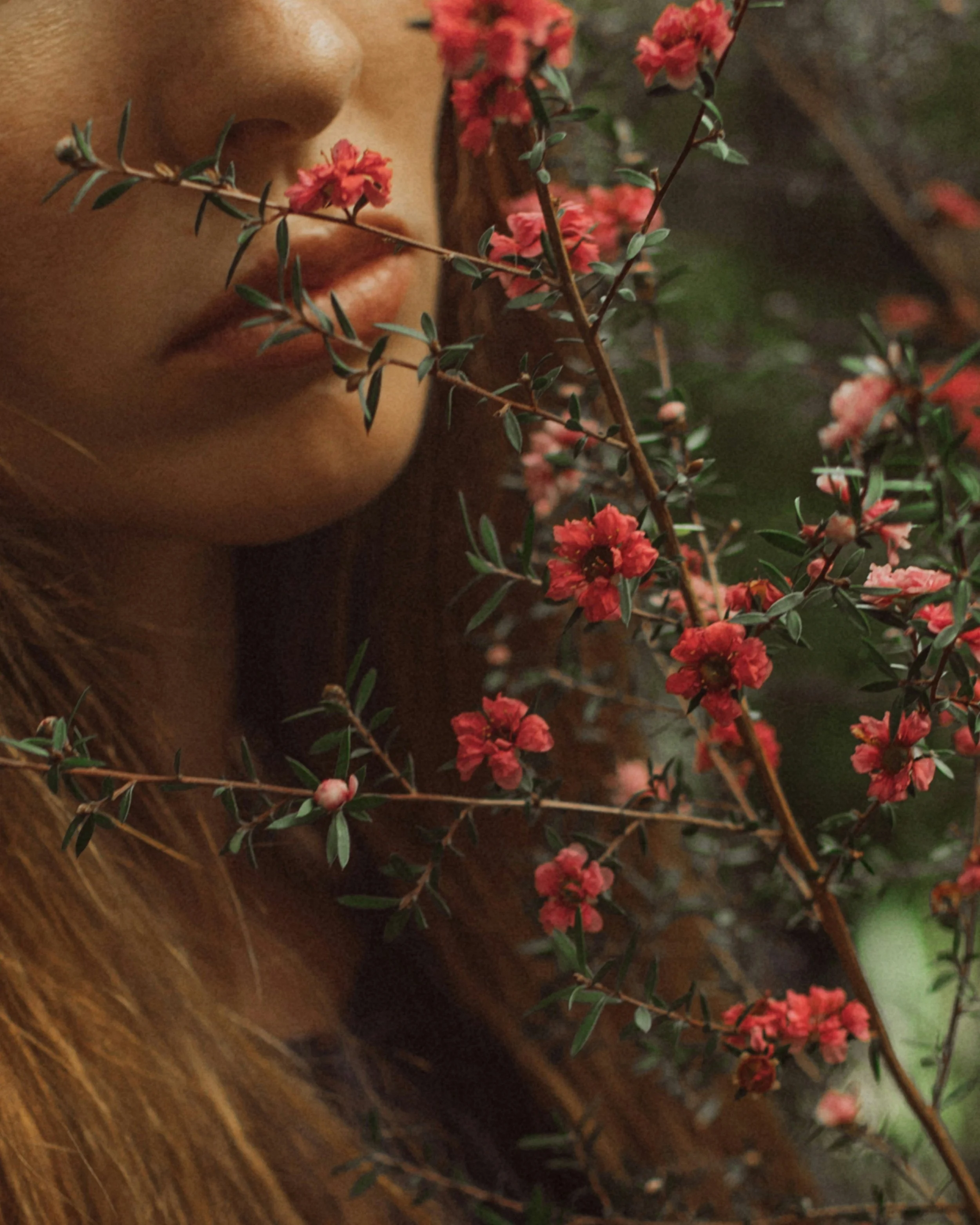 Naheaufnahme eines menschlichen Gesichts mit Fokus auf die Lippen, umgeben von roten Blüten und grünen Blättern.